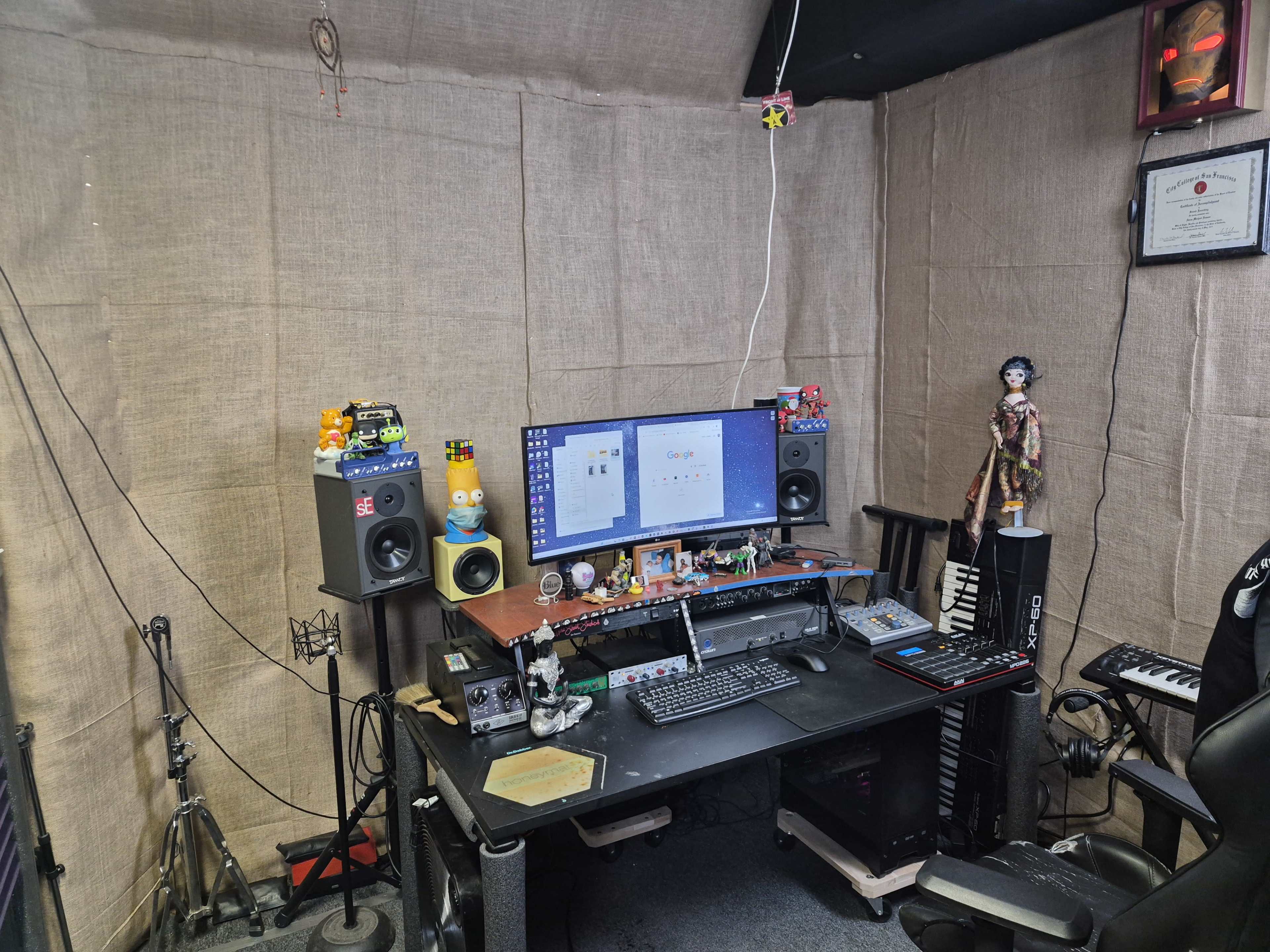 The image shows a home recording studio with a desk featuring a computer monitor, speakers, various musical instruments, and sound equipment, all set against burlap-wrapped walls.