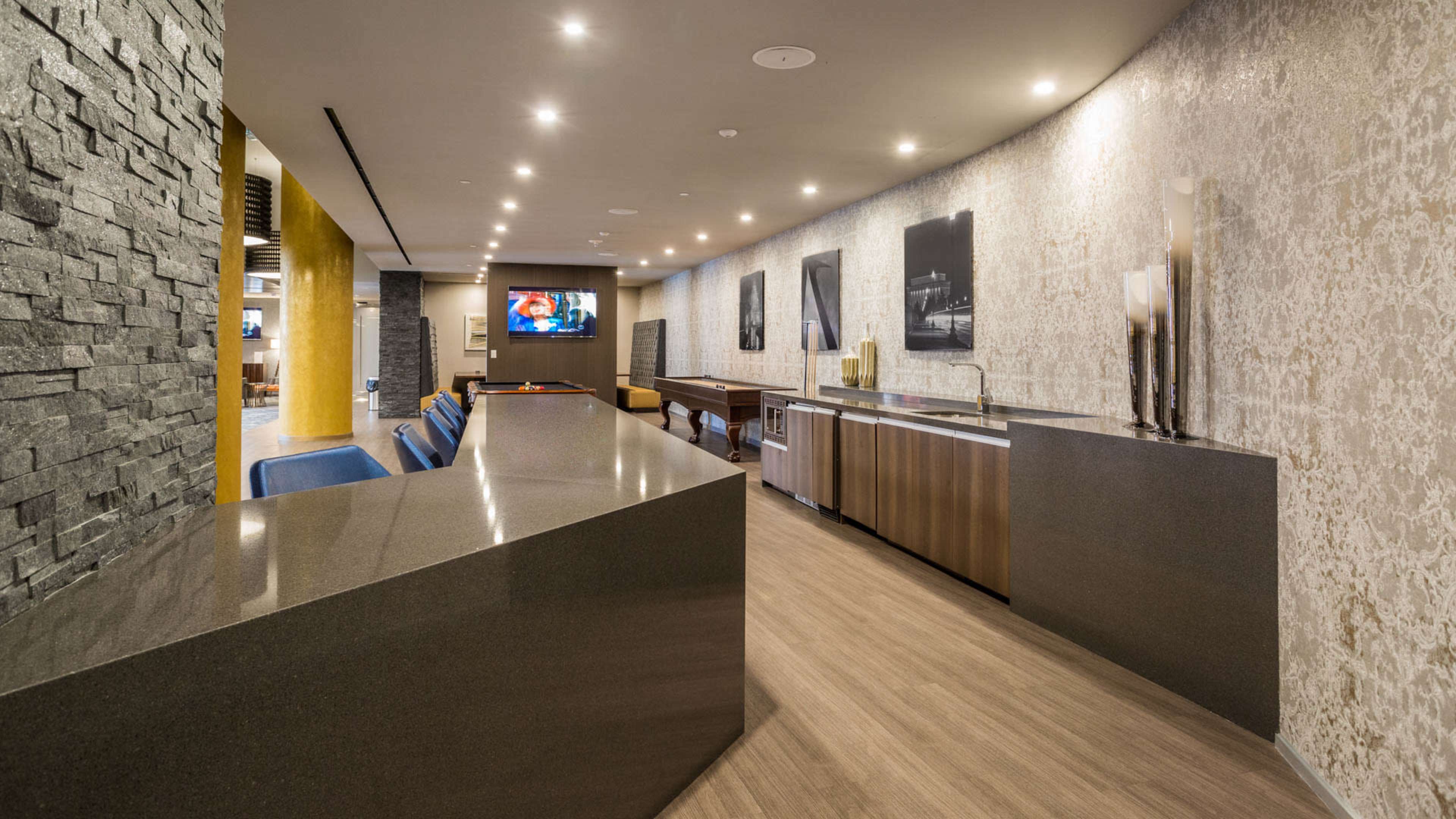 A modern bar area with a sleek countertop, several framed photographs on the walls, and a TV visible in the background.