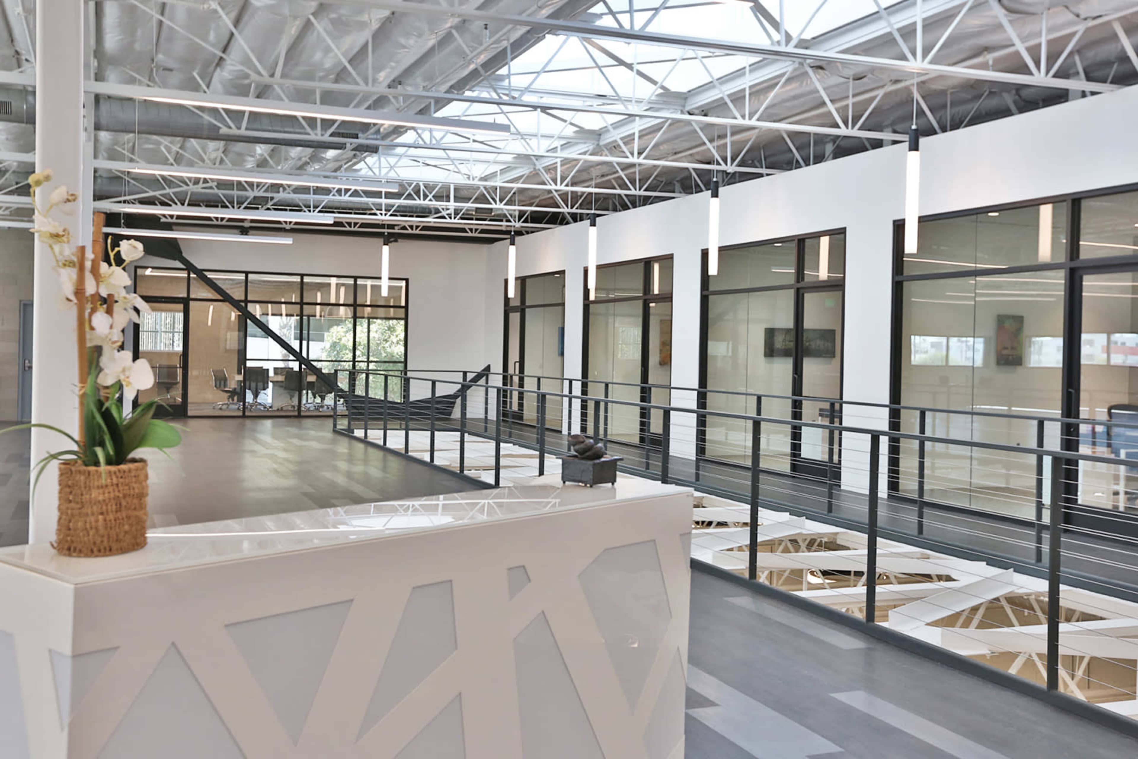 A modern office space with a reception area, large windows, and a balcony overlooking an open area below.