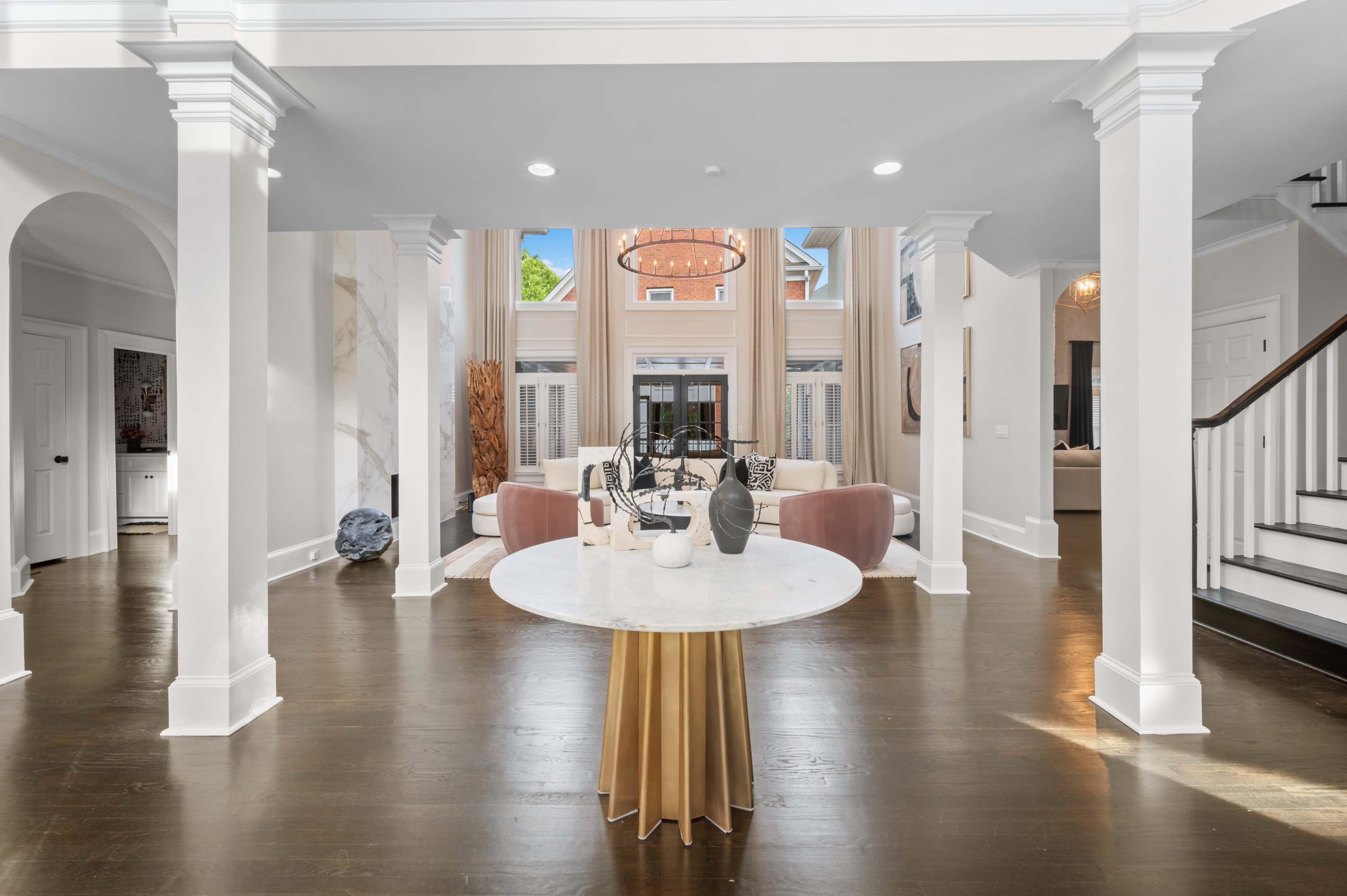 A spacious, open-concept living area with a circular table in the foreground and large windows allowing natural light to fill the space.