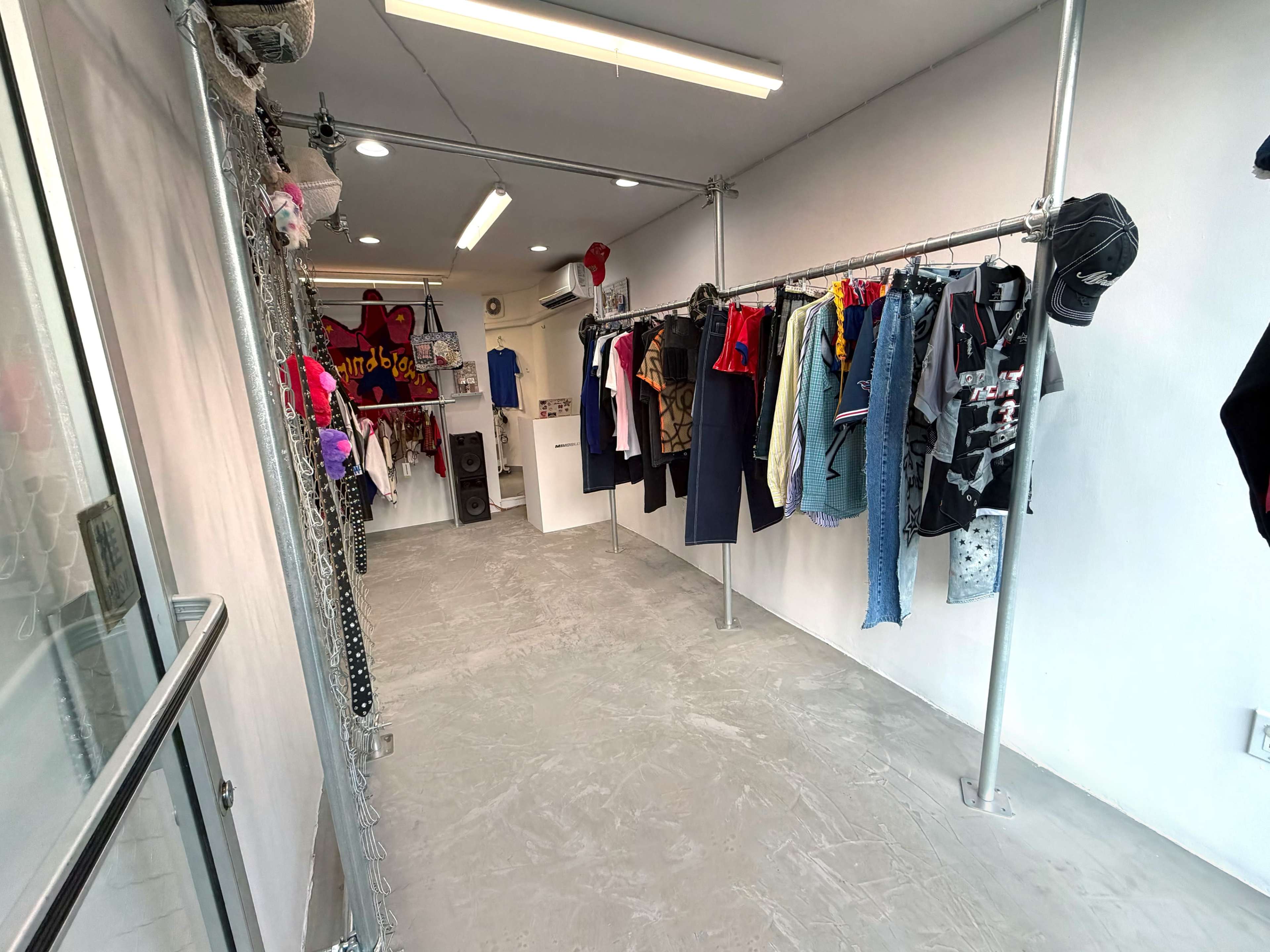 The image shows a narrow clothing retail space with racks displaying various garments along the walls.