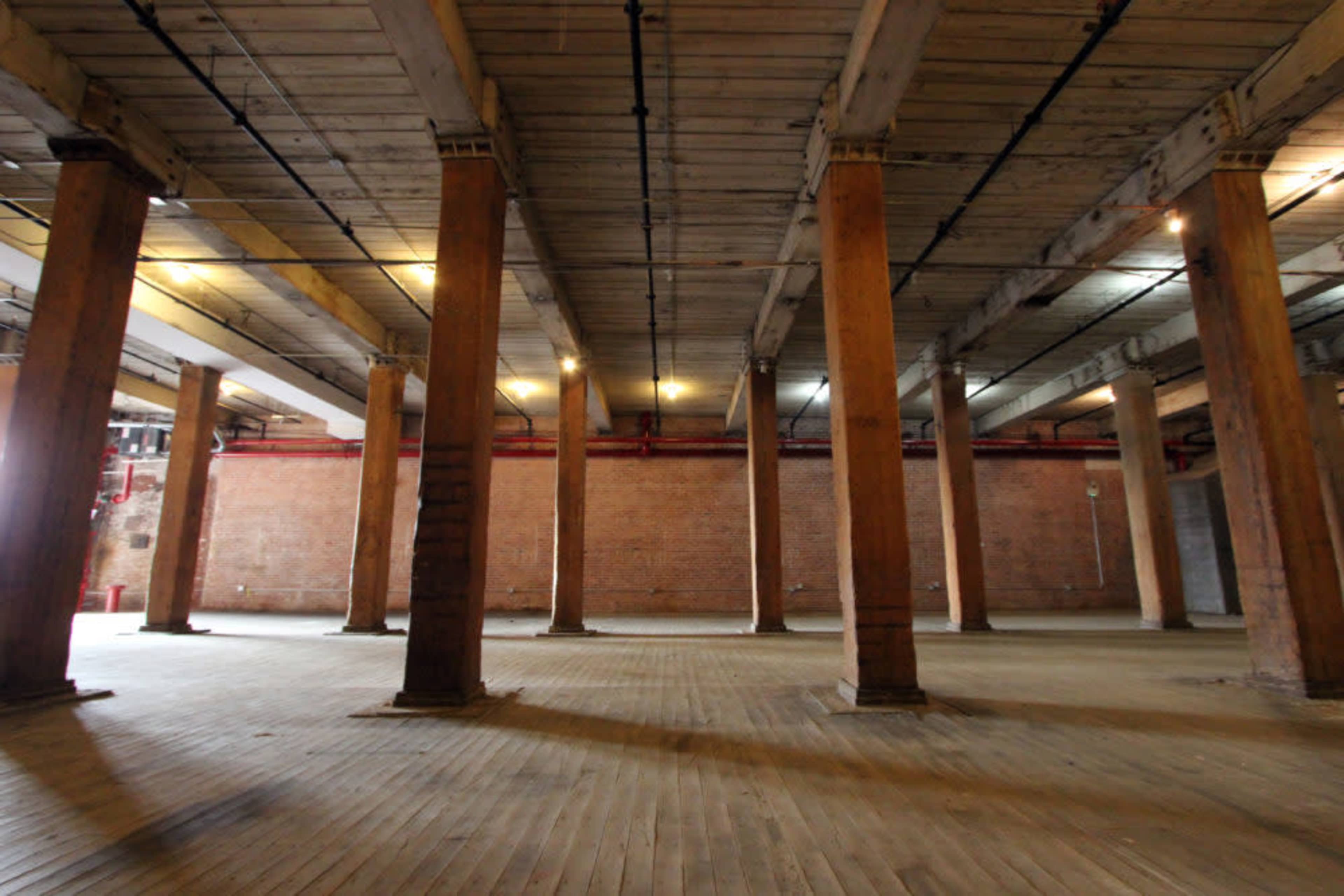 A large, empty industrial space with wooden floors and columns supporting the ceiling.