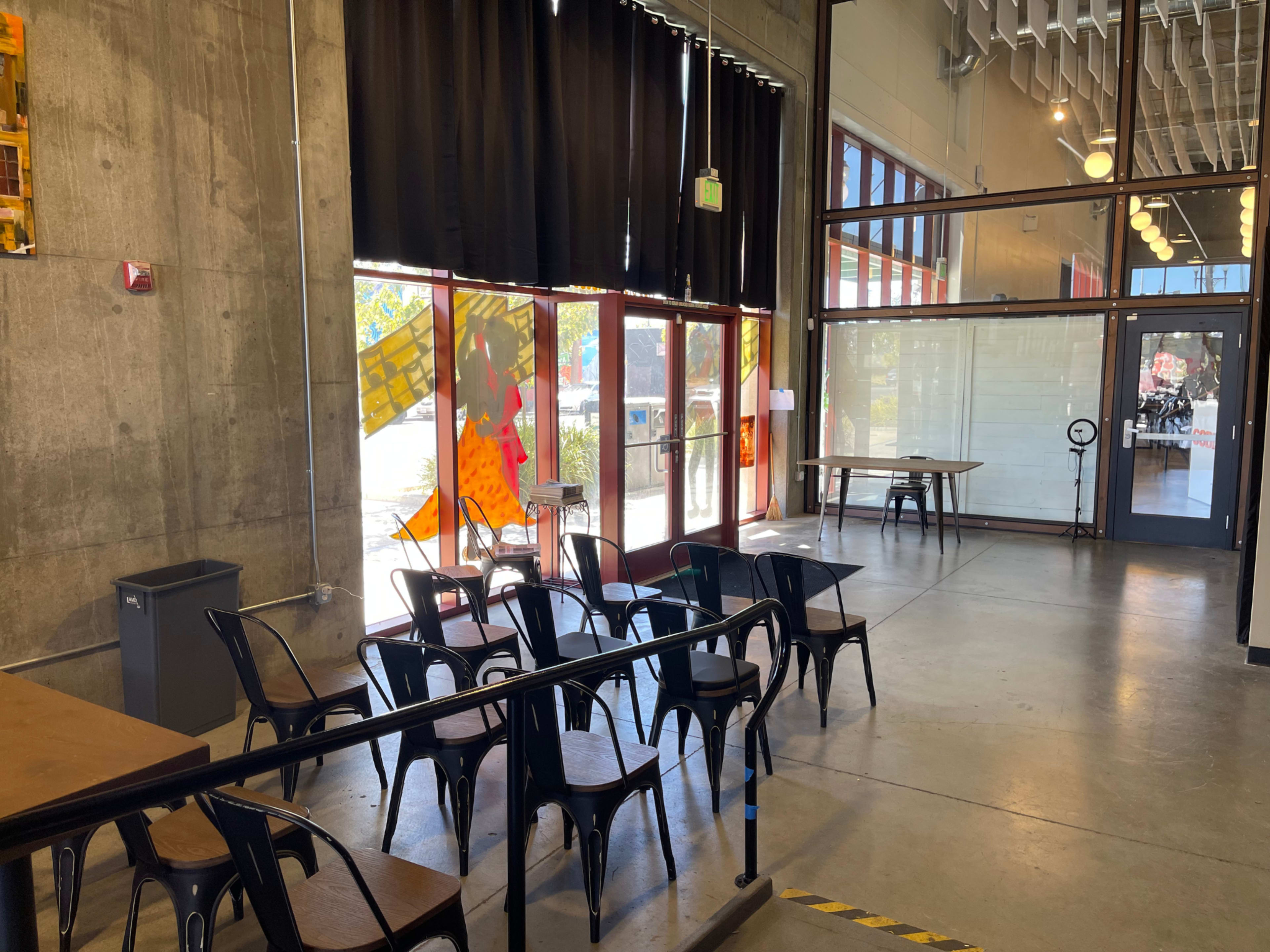 The image shows a spacious interior with metal chairs arranged facing a large window, which lets in natural light.
