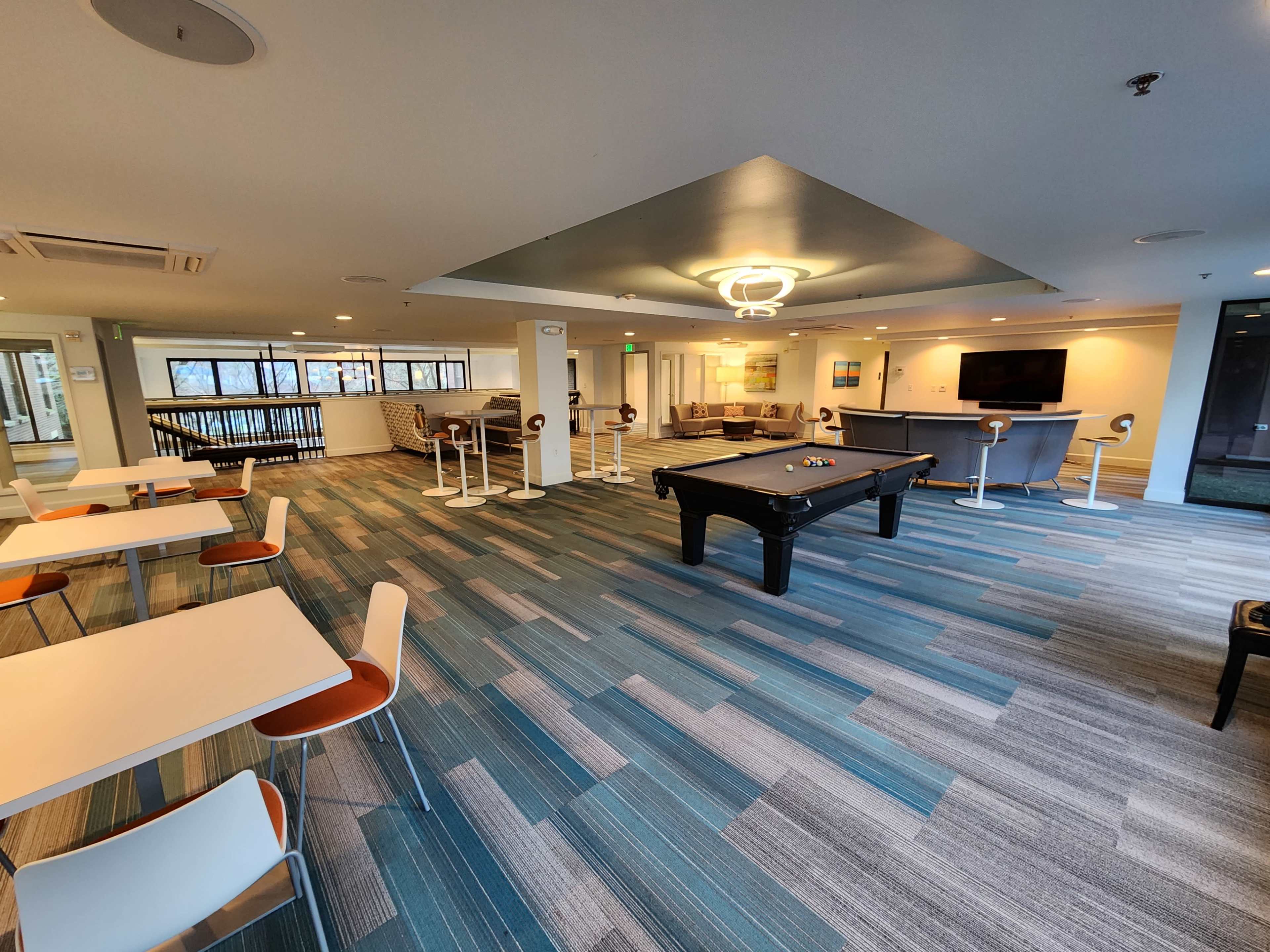 A lounge area featuring a pool table, several tables with chairs, and a seating area with modern furnishings.