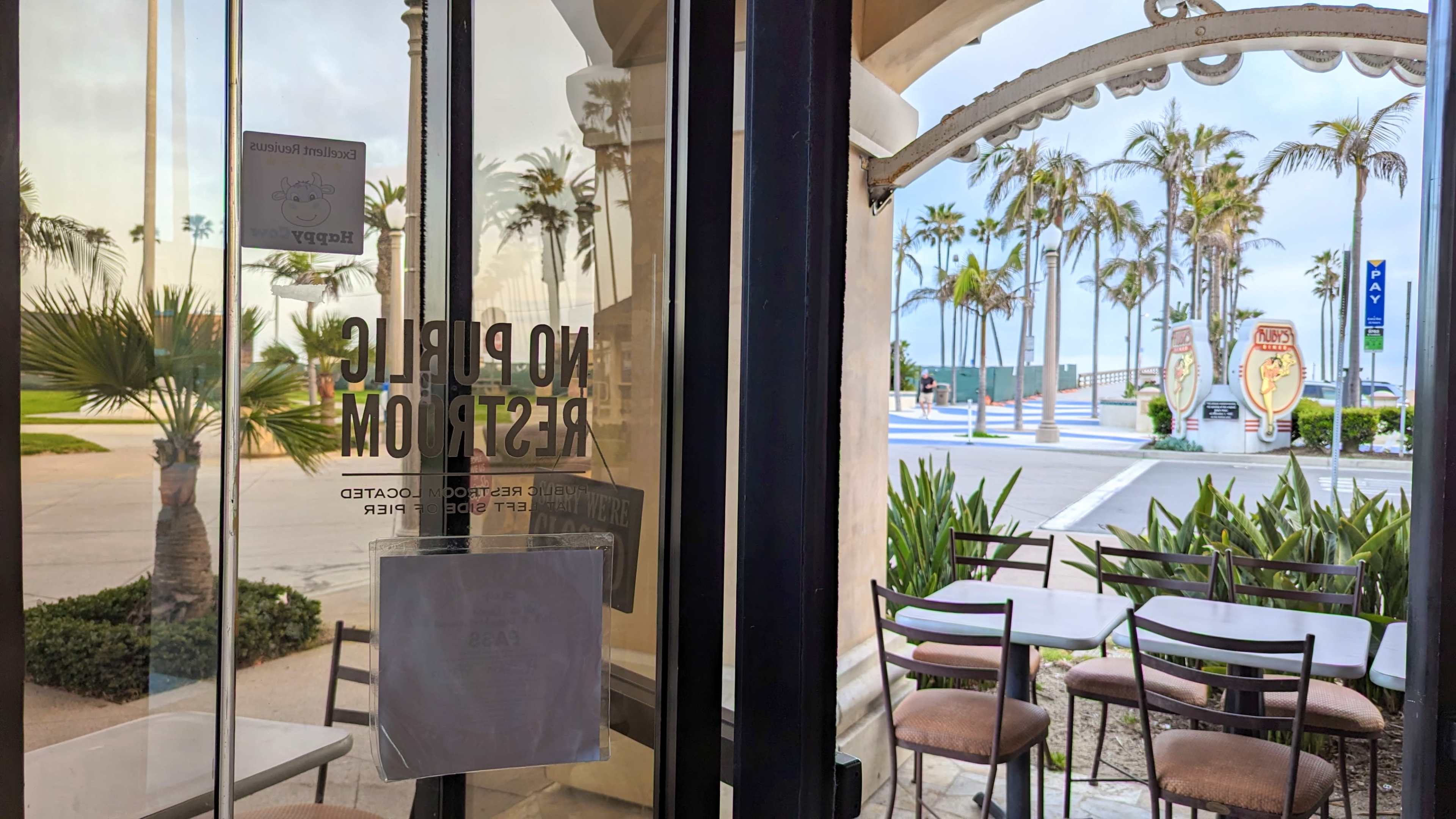 An open doorway leading to a beachfront with palm trees and a few tables and chairs arranged inside a café.