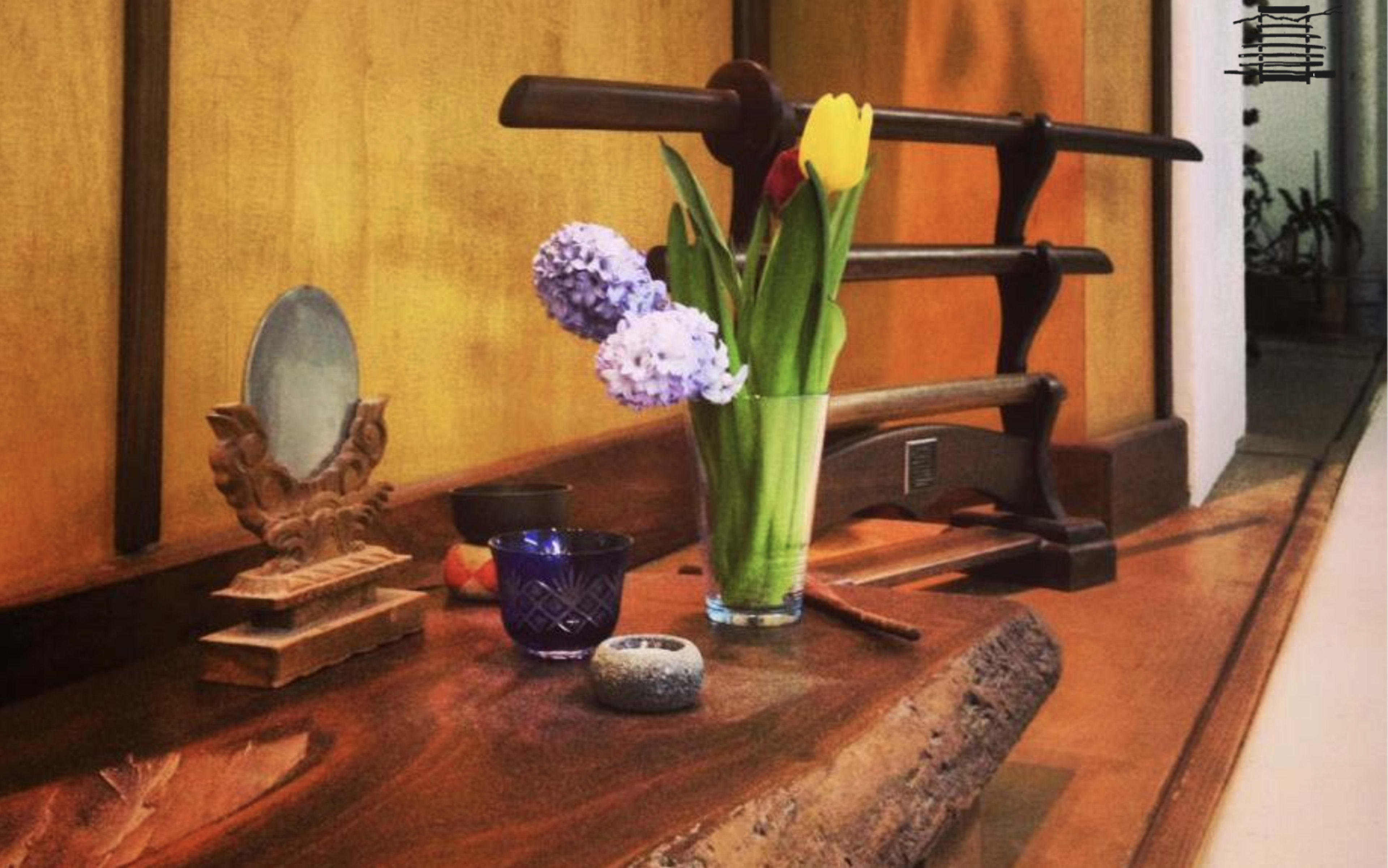 A wooden tabletop displays a vase of tulips and hyacinths alongside decorative objects and a display stand for a katana.