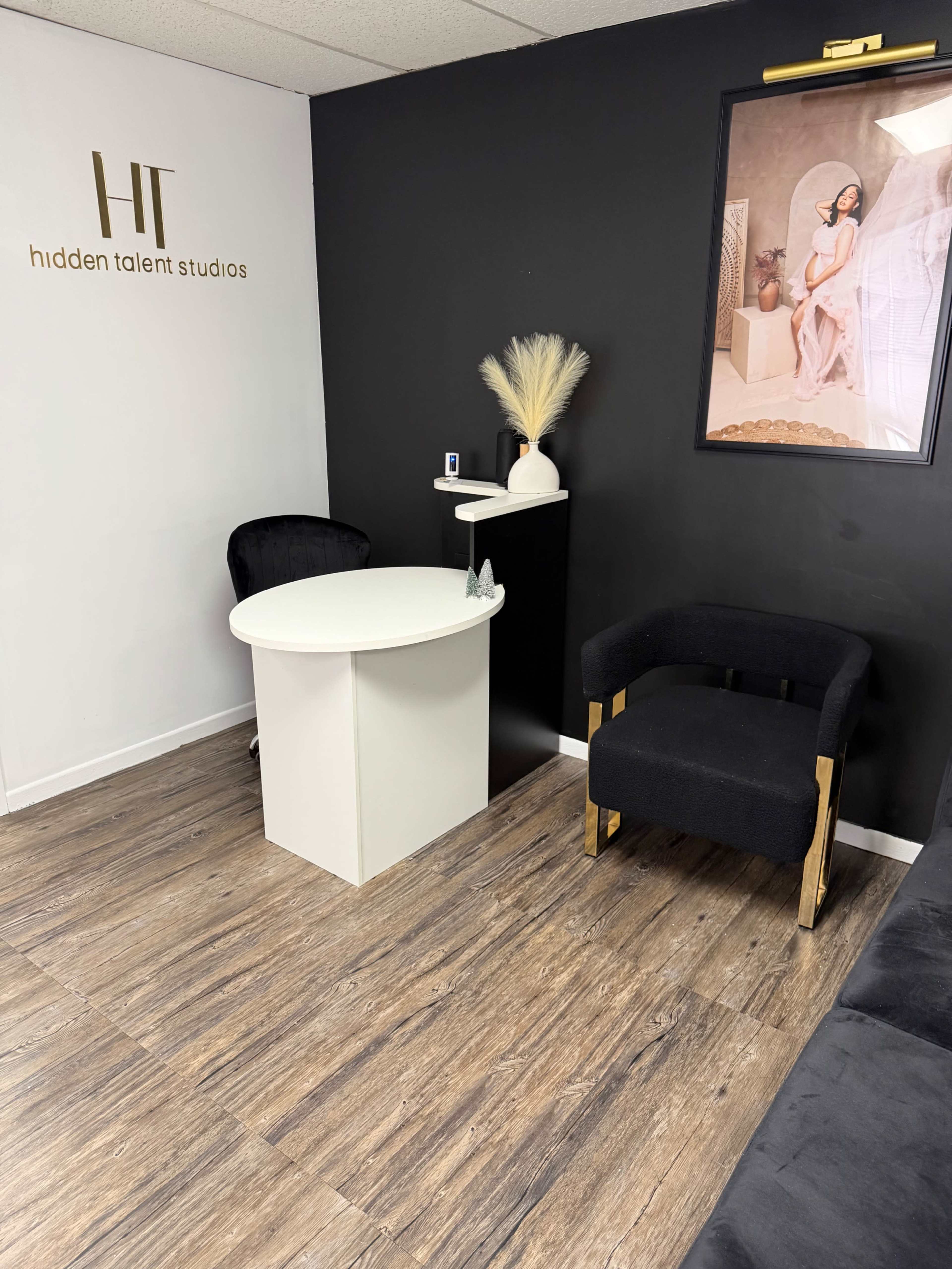 The image displays a modern reception area featuring a round white desk, a black armchair, and a wall adorned with a framed photo and decorative elements.