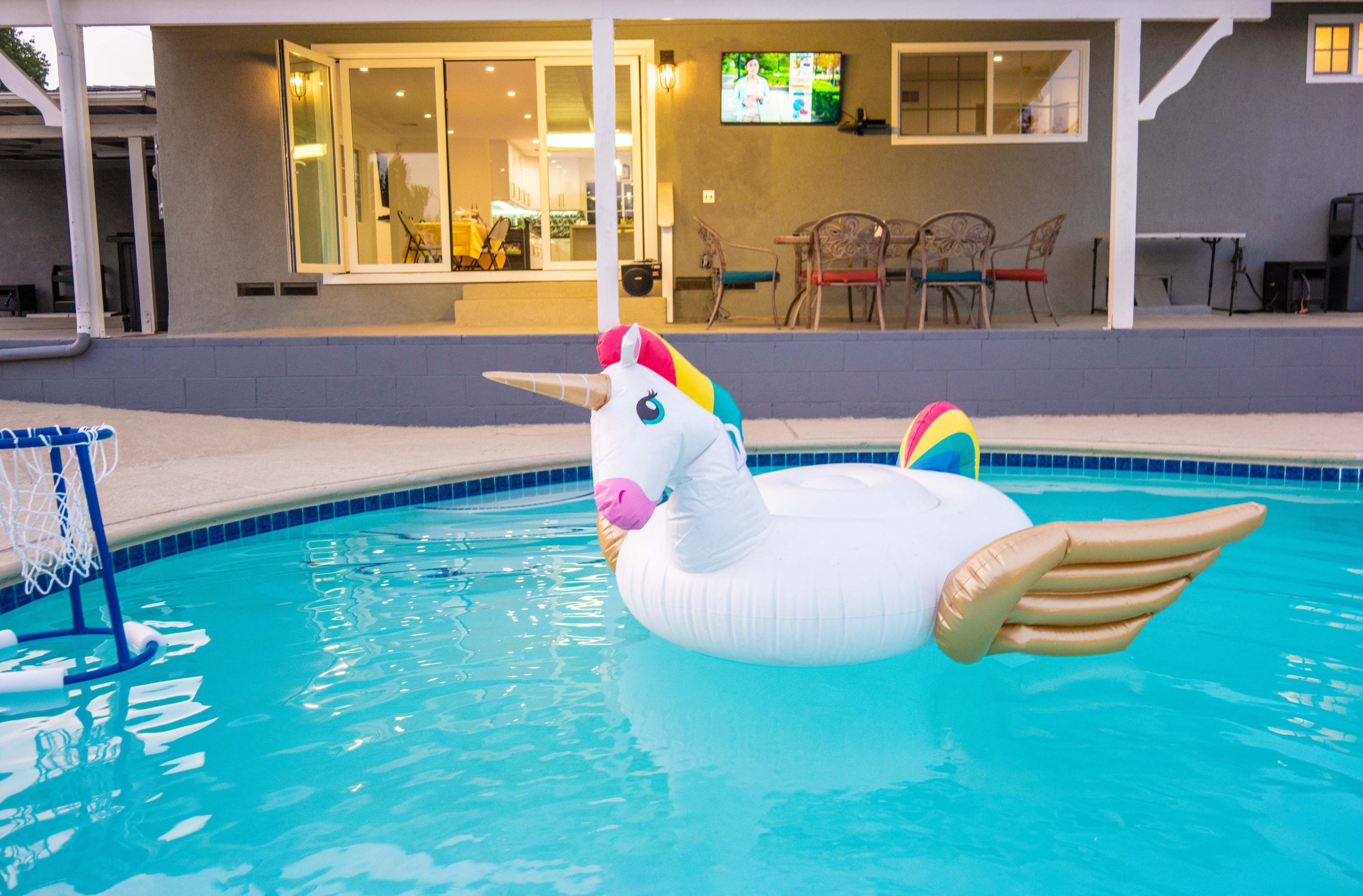 A large inflatable unicorn float is positioned in a swimming pool, with a modern home and patio visible in the background.