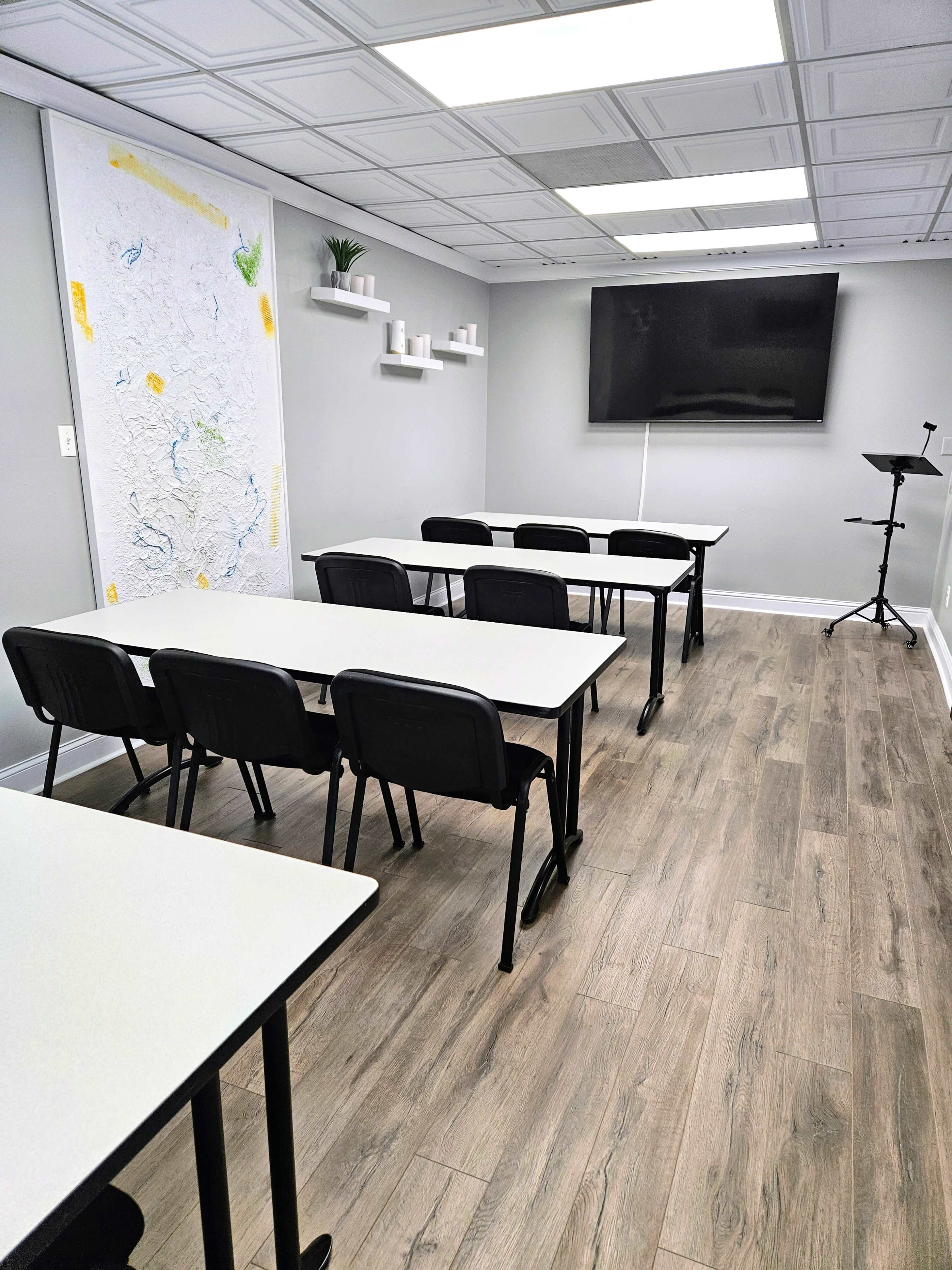 A modern classroom setup with rows of white tables and black chairs, a large screen on the wall, and minimalistic decor.