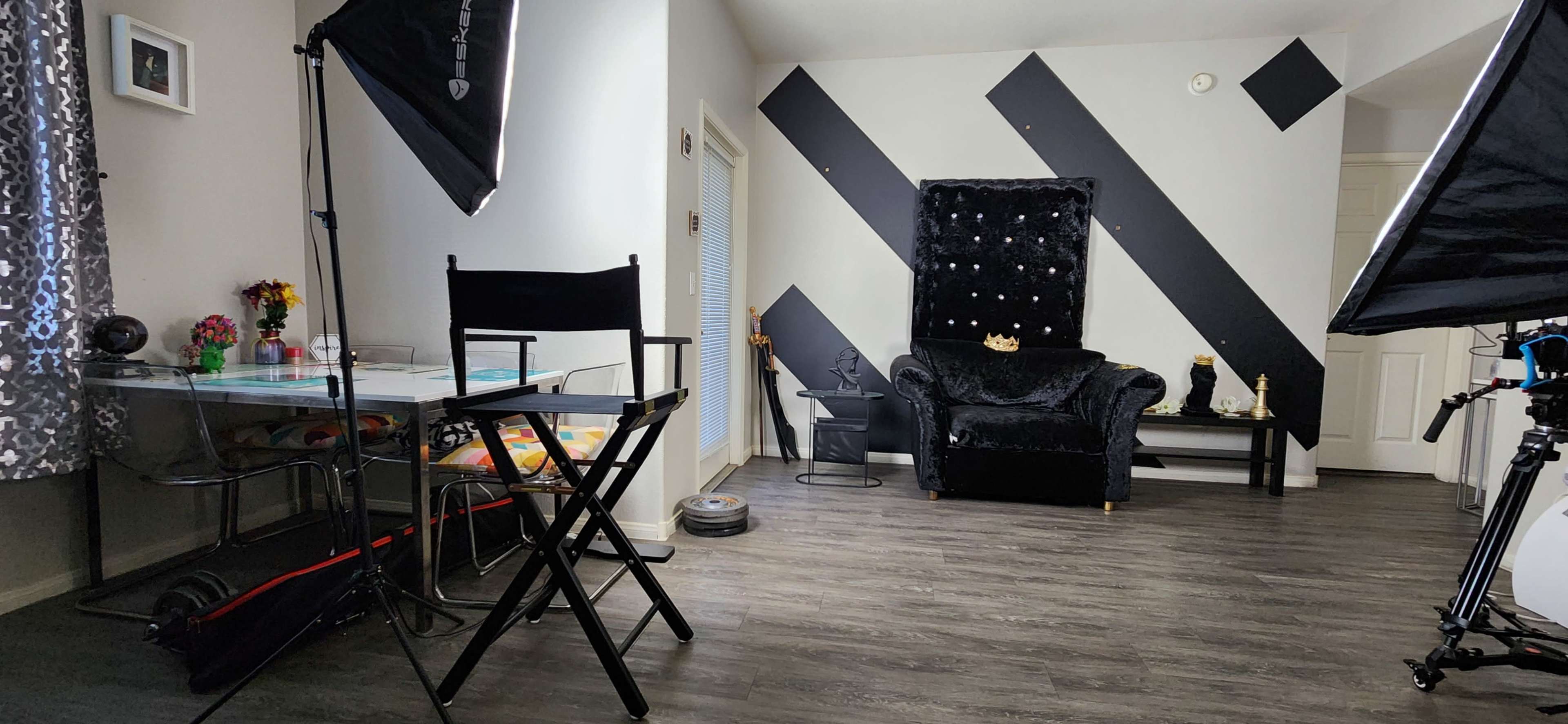 A brightly lit room featuring a black velvet chair, a glass table, and two photographic lighting setups.