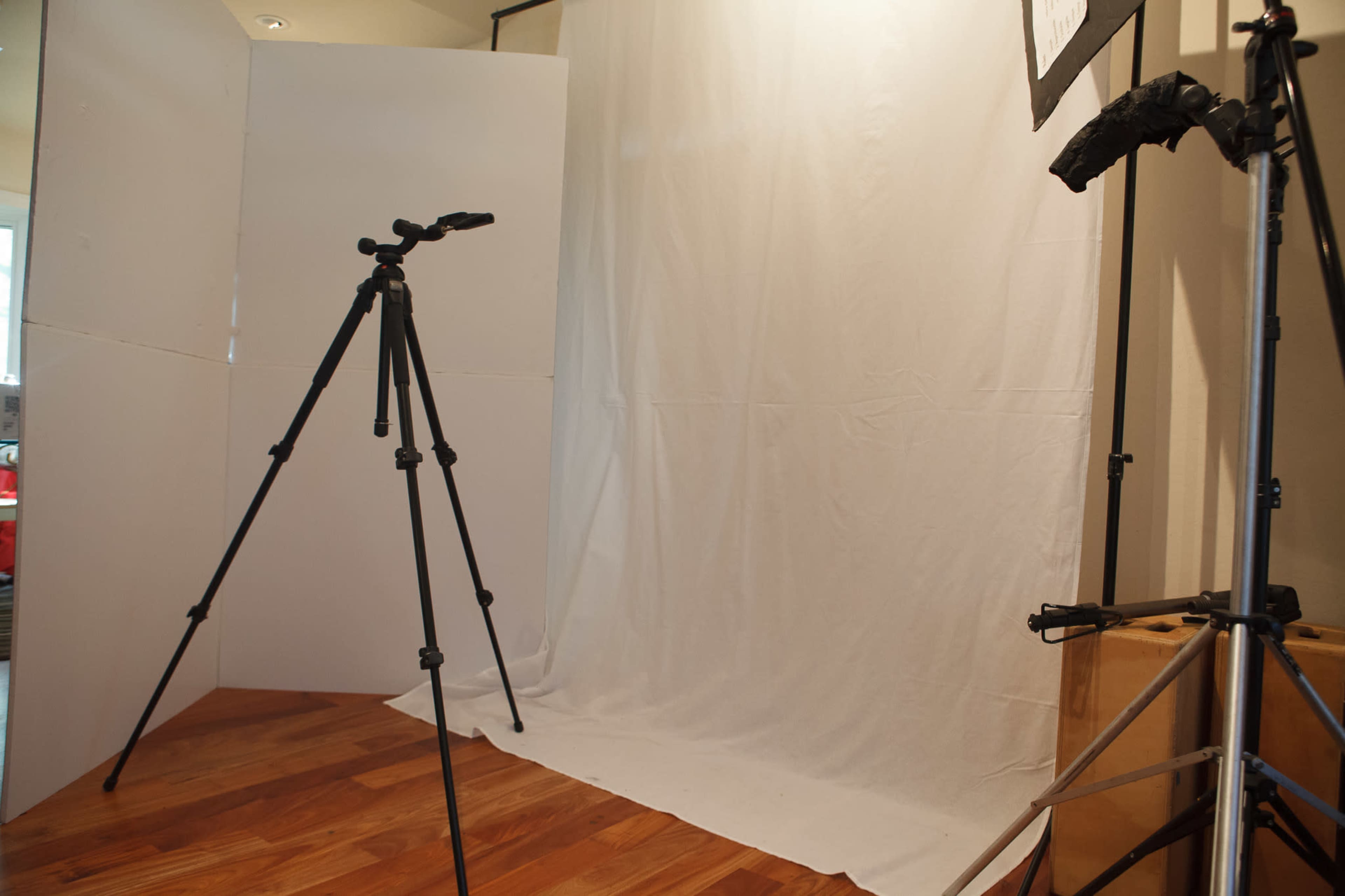 The image shows a simple photography setup with two tripods positioned in front of a white backdrop.