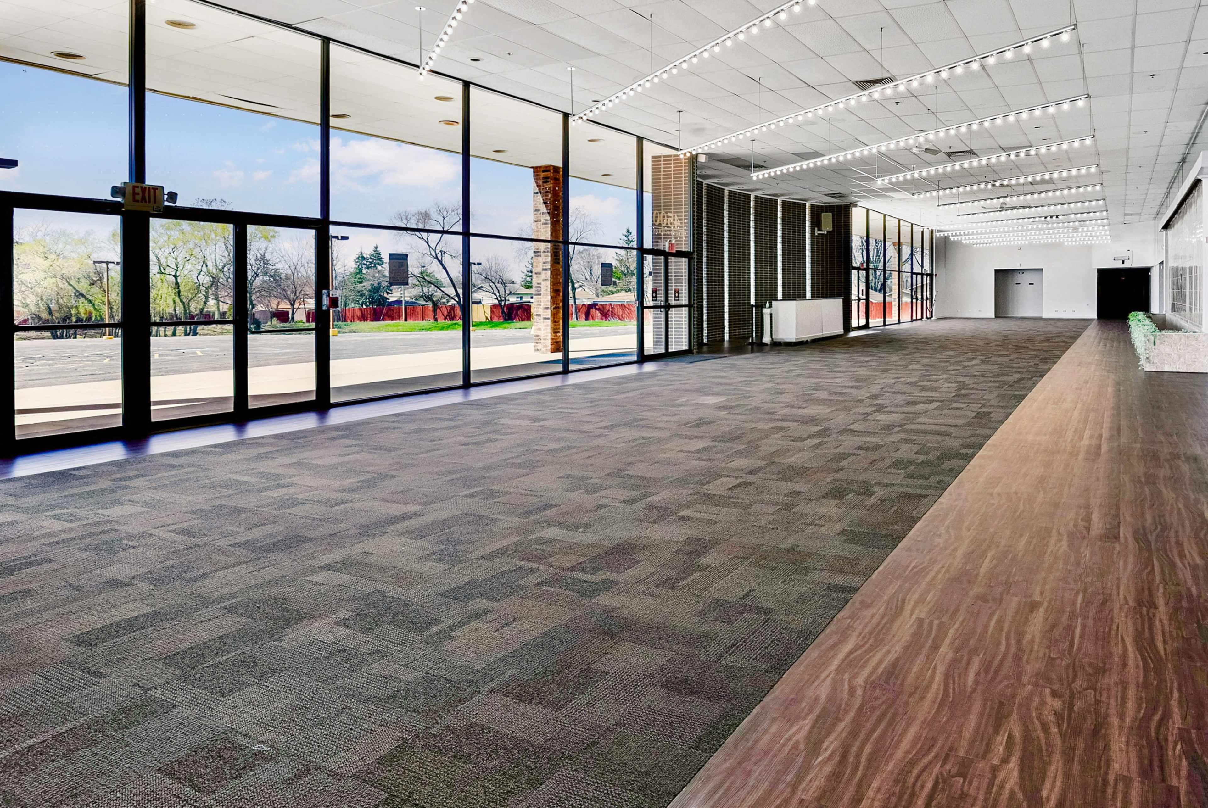 A spacious, well-lit interior area with large windows and a mix of carpet and wood flooring.