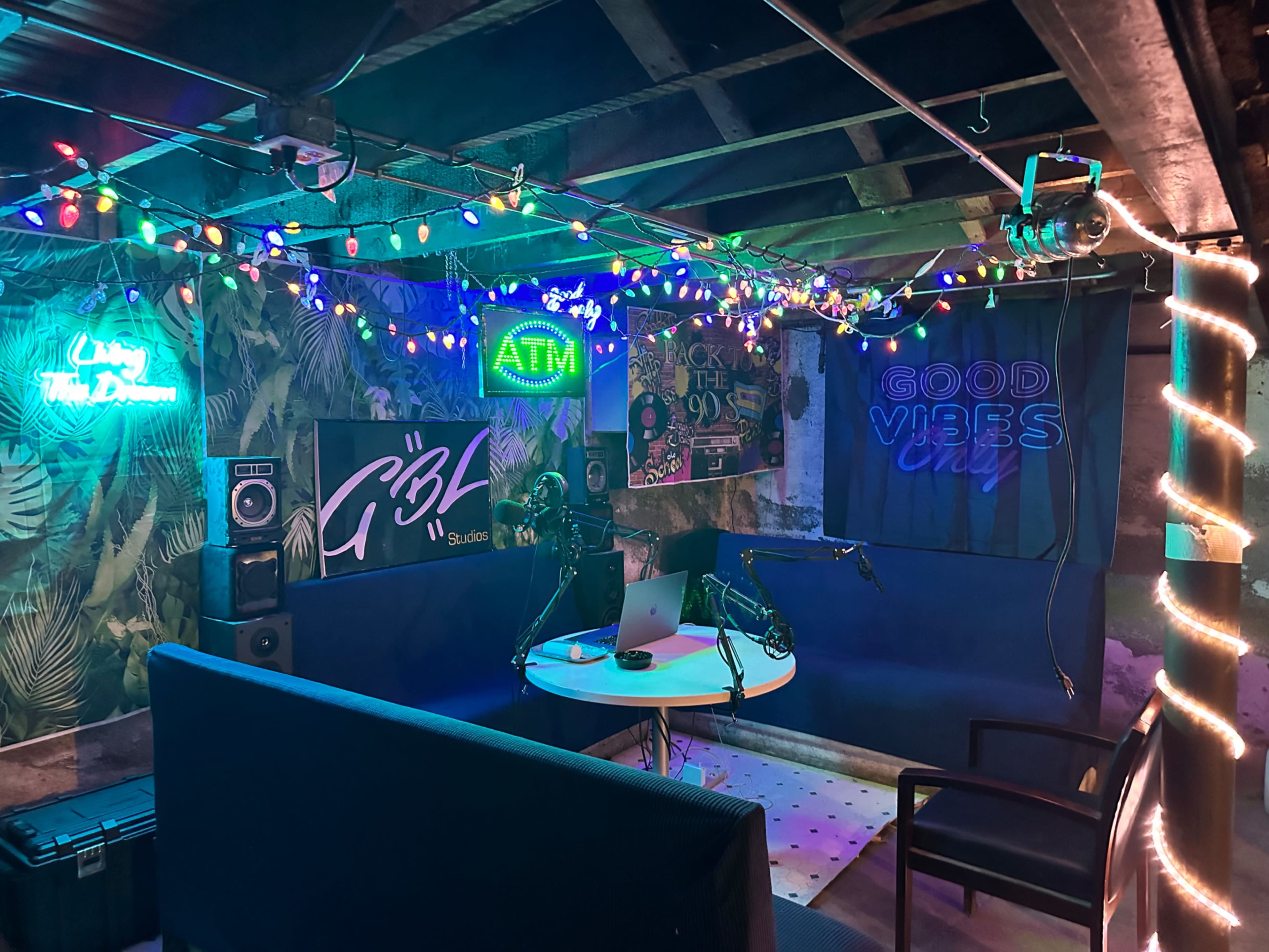 A colorful, dimly lit recording studio featuring string lights, a circular table with a microphone, and various decorative elements on the walls.