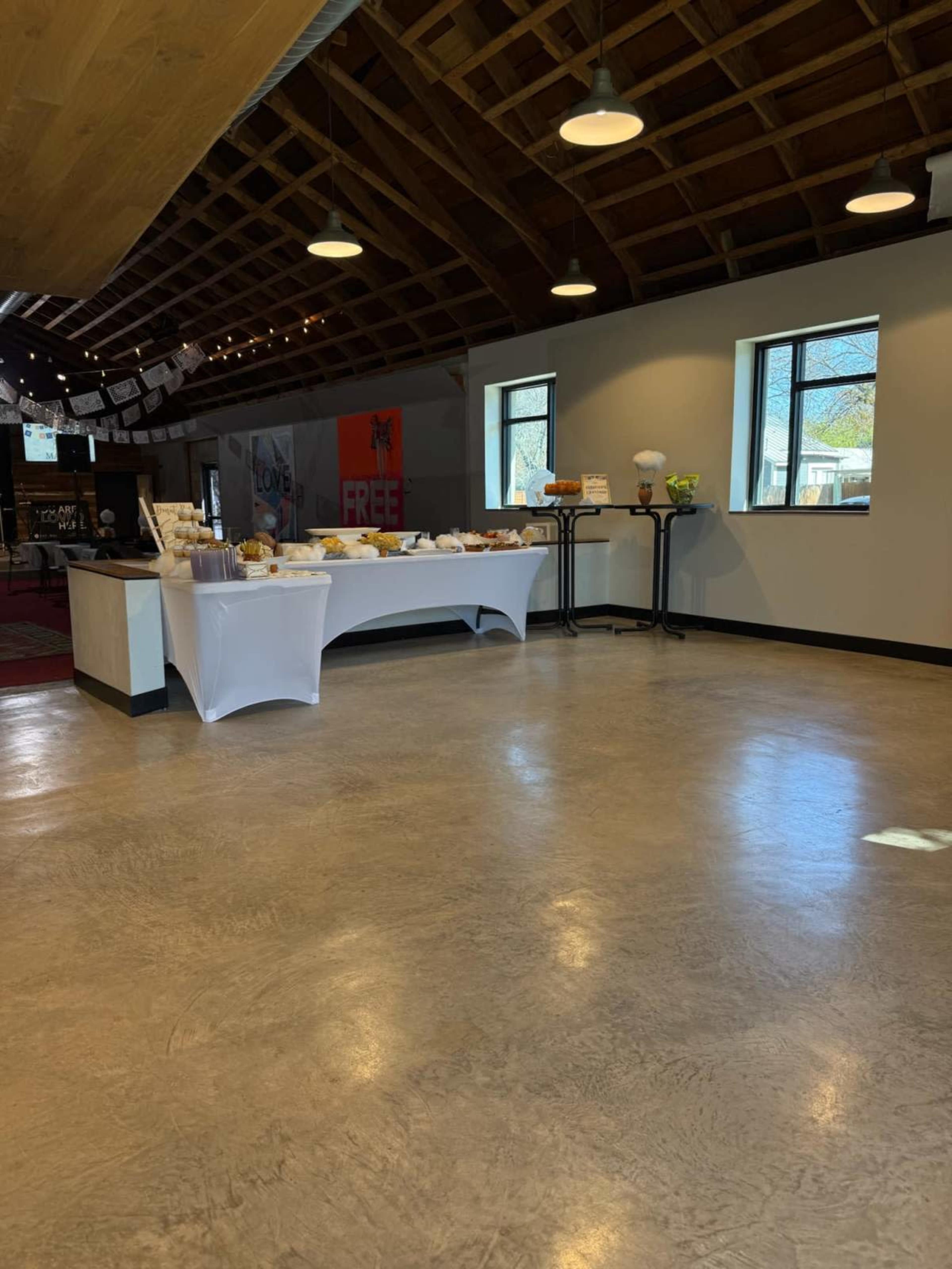 The image shows a spacious indoor area with a long table covered in food items and bright overhead lights.