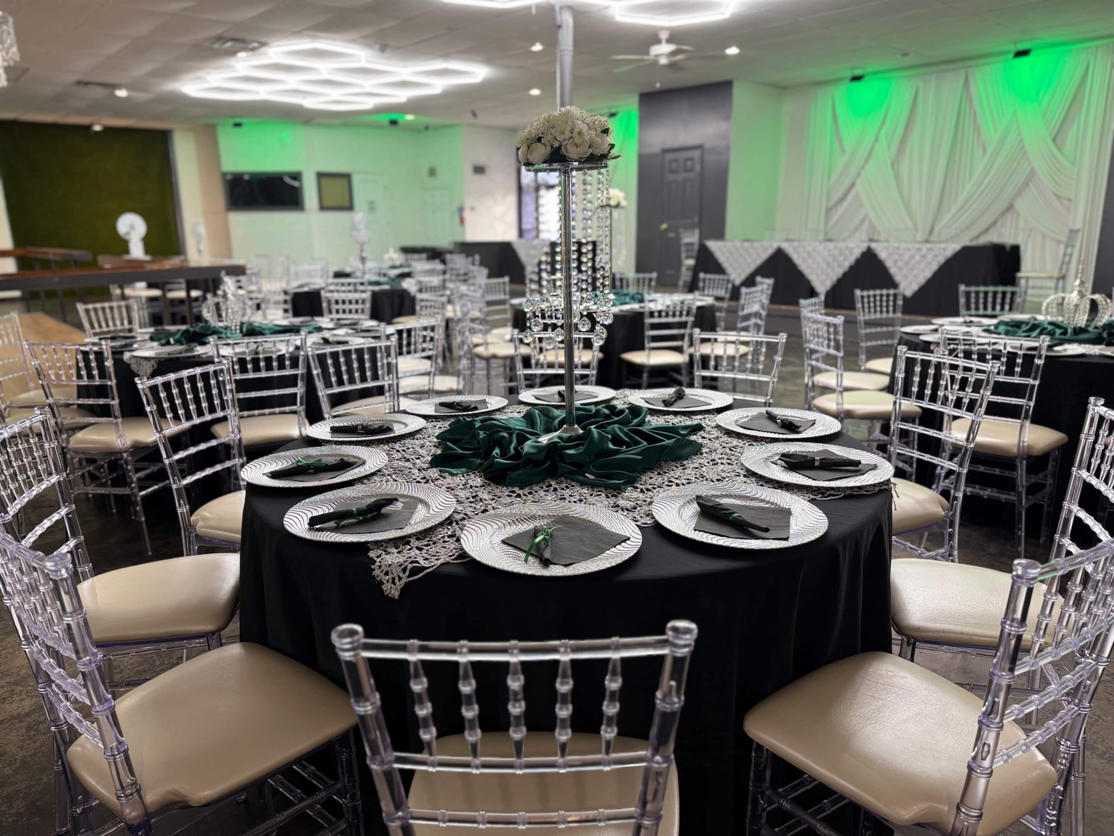 A banquet hall is set up with several tables adorned in black tablecloths, each featuring decorative centerpieces and place settings.