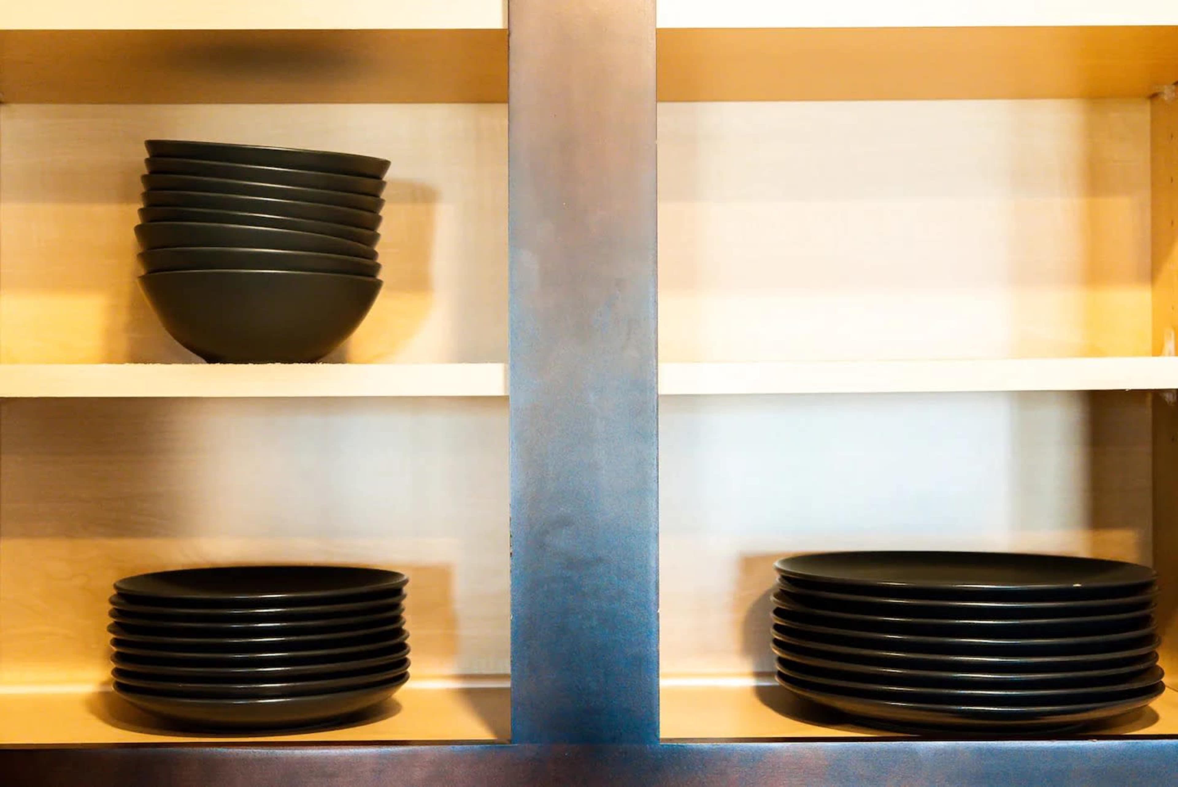 A set of black dishes is neatly arranged on wooden shelves, with bowls on the top shelf and plates on the bottom shelf.
