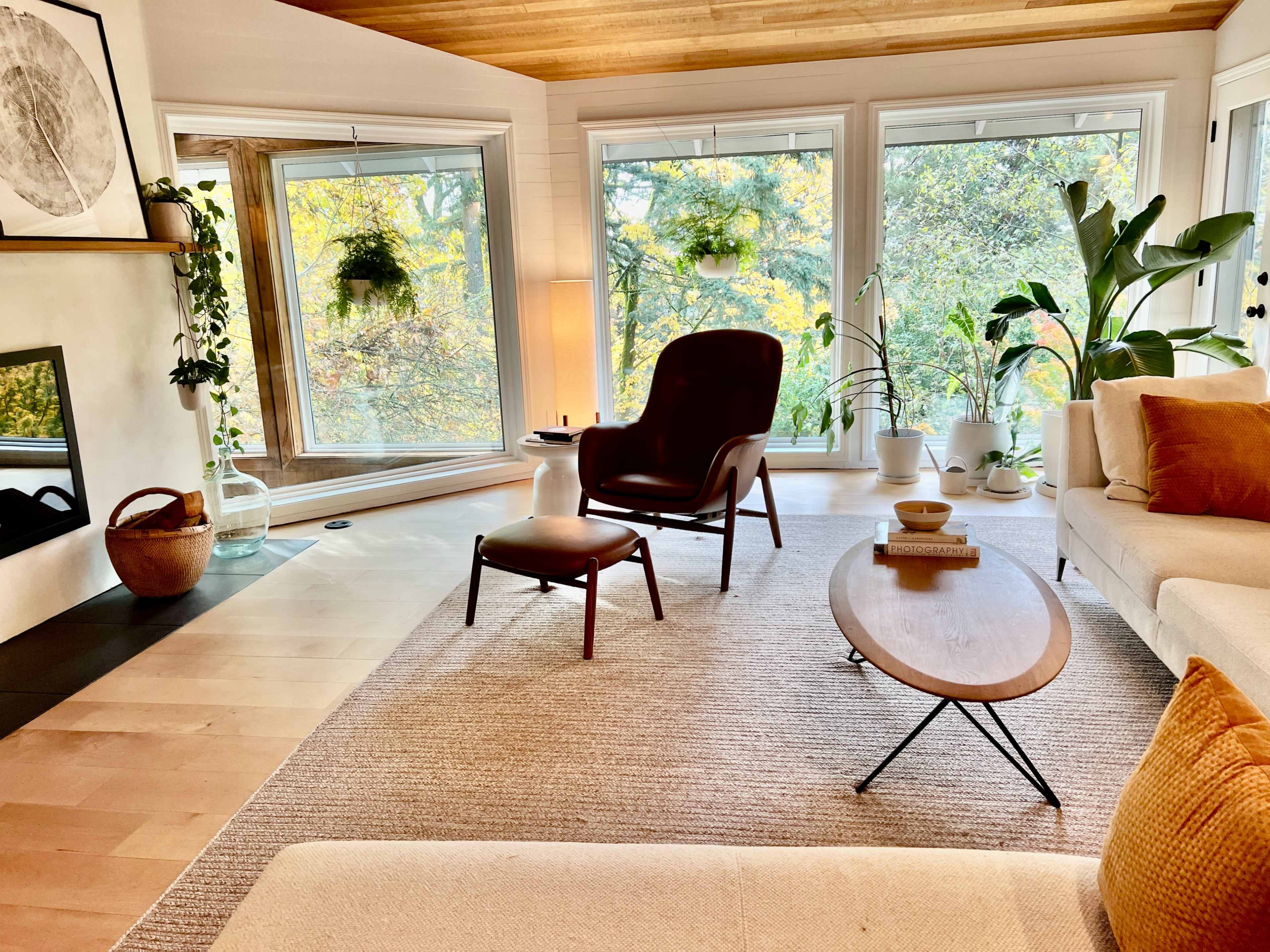 A modern living room features a comfortable armchair and ottoman, a coffee table, and large windows showcasing greenery outside.