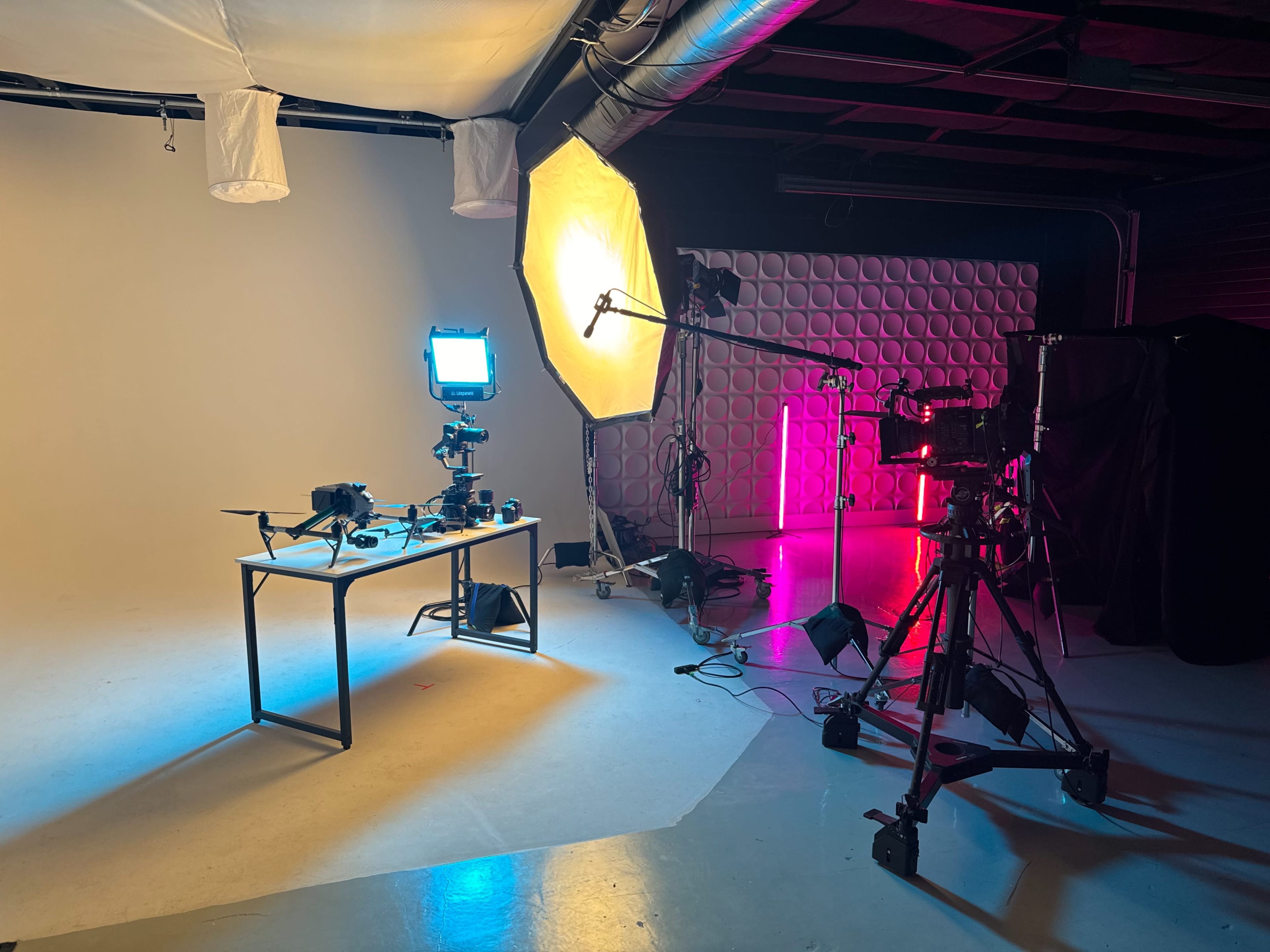 A film set is arranged with a table displaying equipment, two softbox lights, and a camera on a tripod in a studio space.