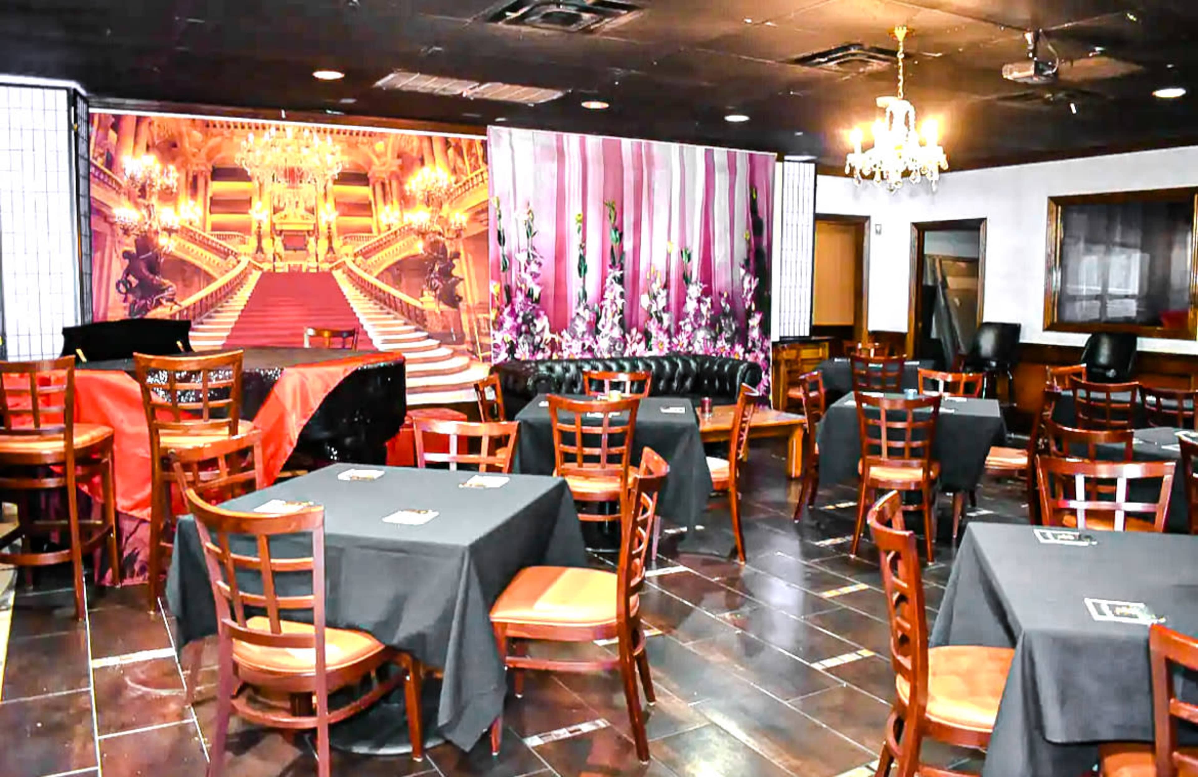 An empty restaurant with tables covered in black cloth and a large mural of an ornate staircase on the back wall.