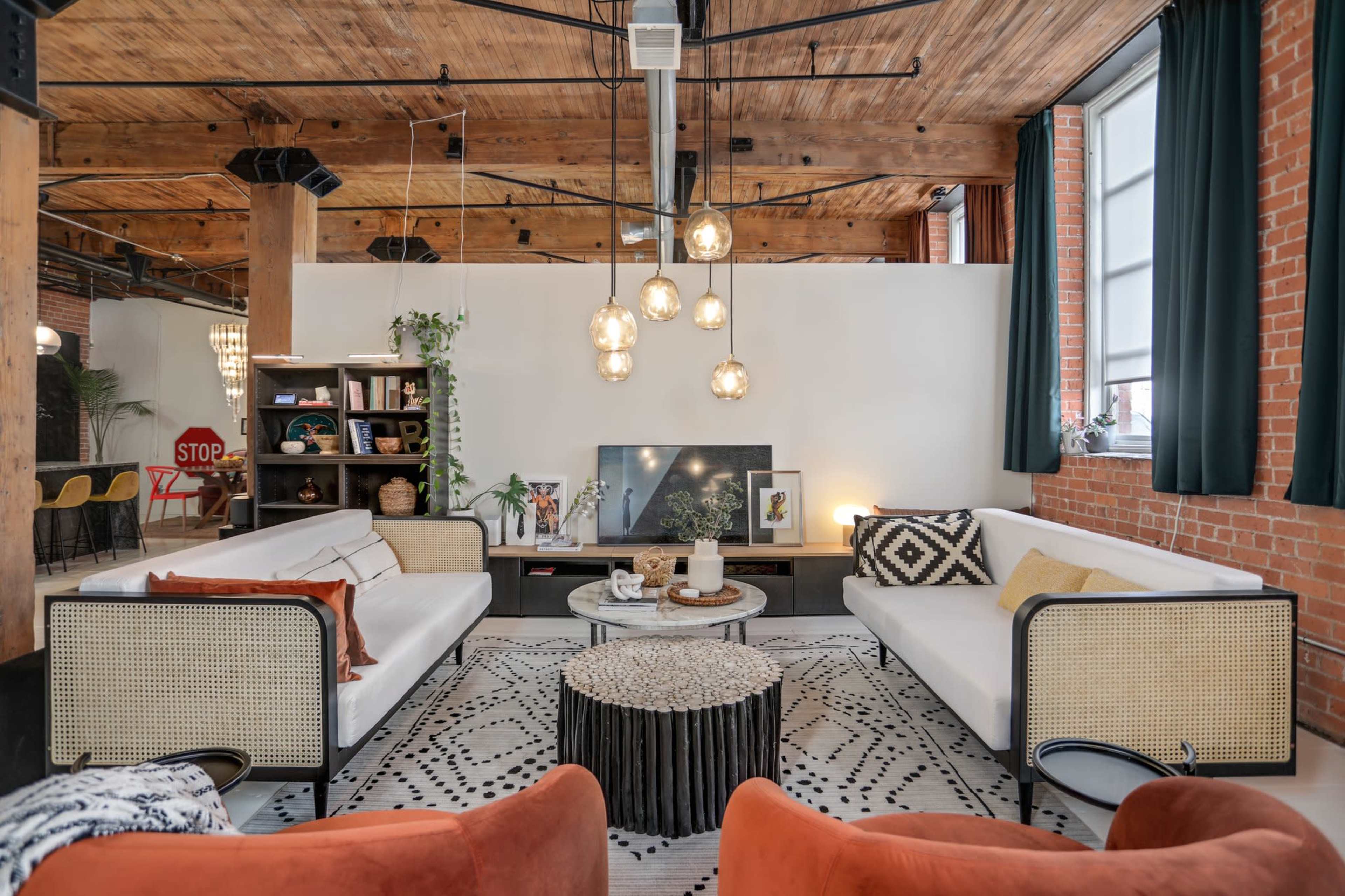 A modern living room with white sofas, a circular coffee table on a patterned rug, and exposed brick walls and wooden beams.