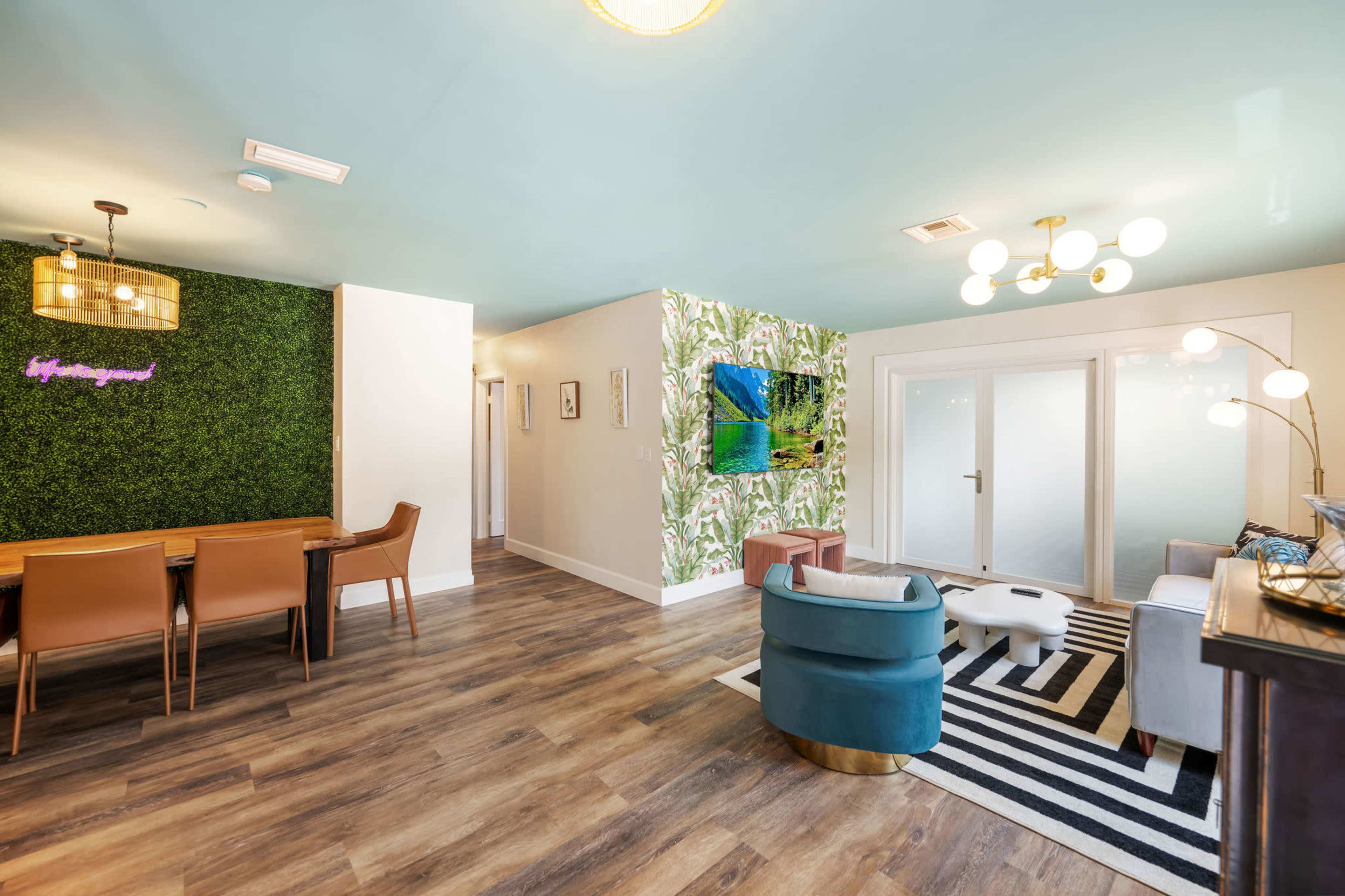 A modern living area with a green wall feature, a dining table, and decorative elements, including a large piece of artwork.