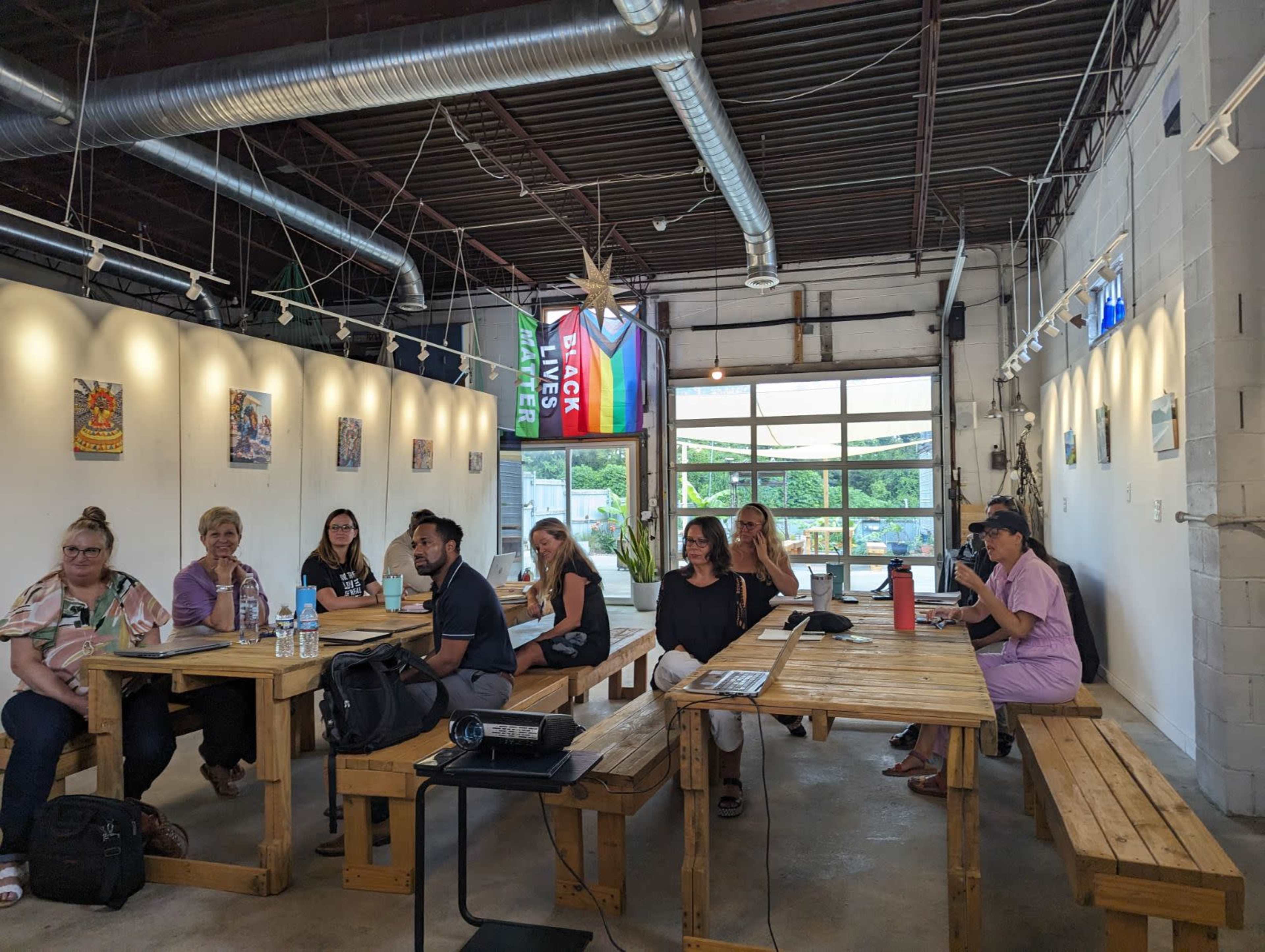 A group of people is seated at wooden tables in a well-lit room with artwork on the walls and flags hanging from the ceiling.