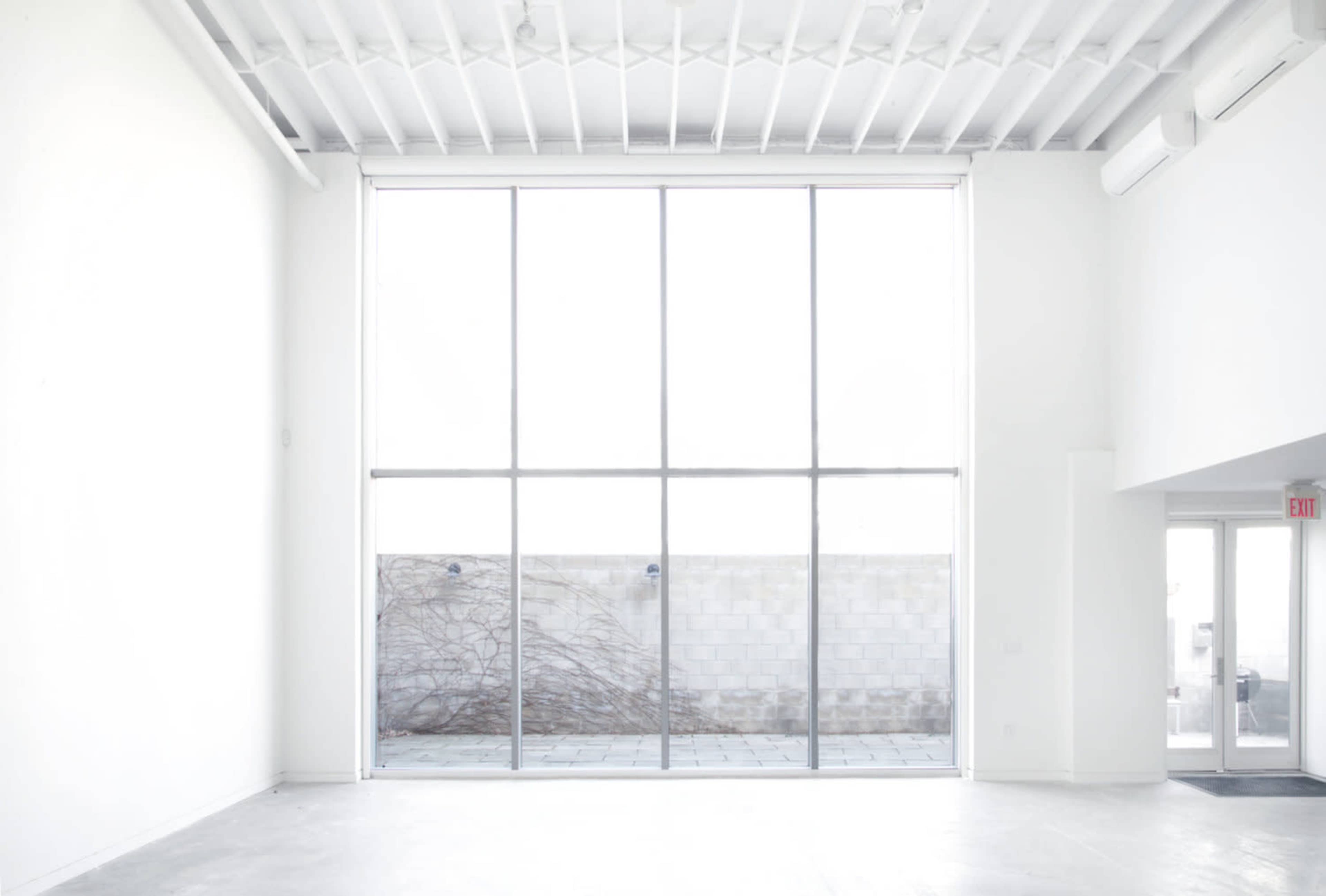 A minimalist interior with large glass windows overlooking a bare outdoor space.