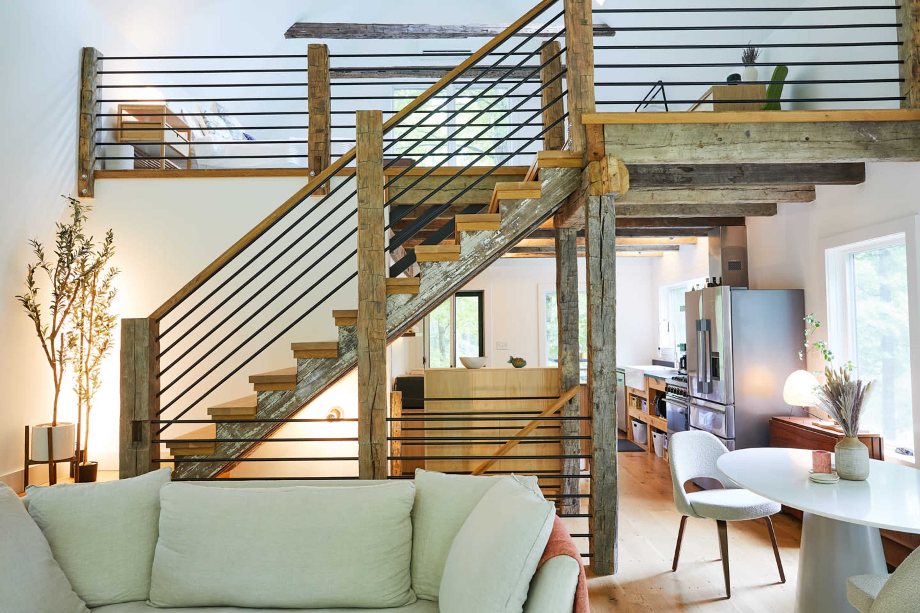 A modern interior featuring a wooden staircase with metal railings, leading to an upper level, with an open kitchen and living area visible in the background.