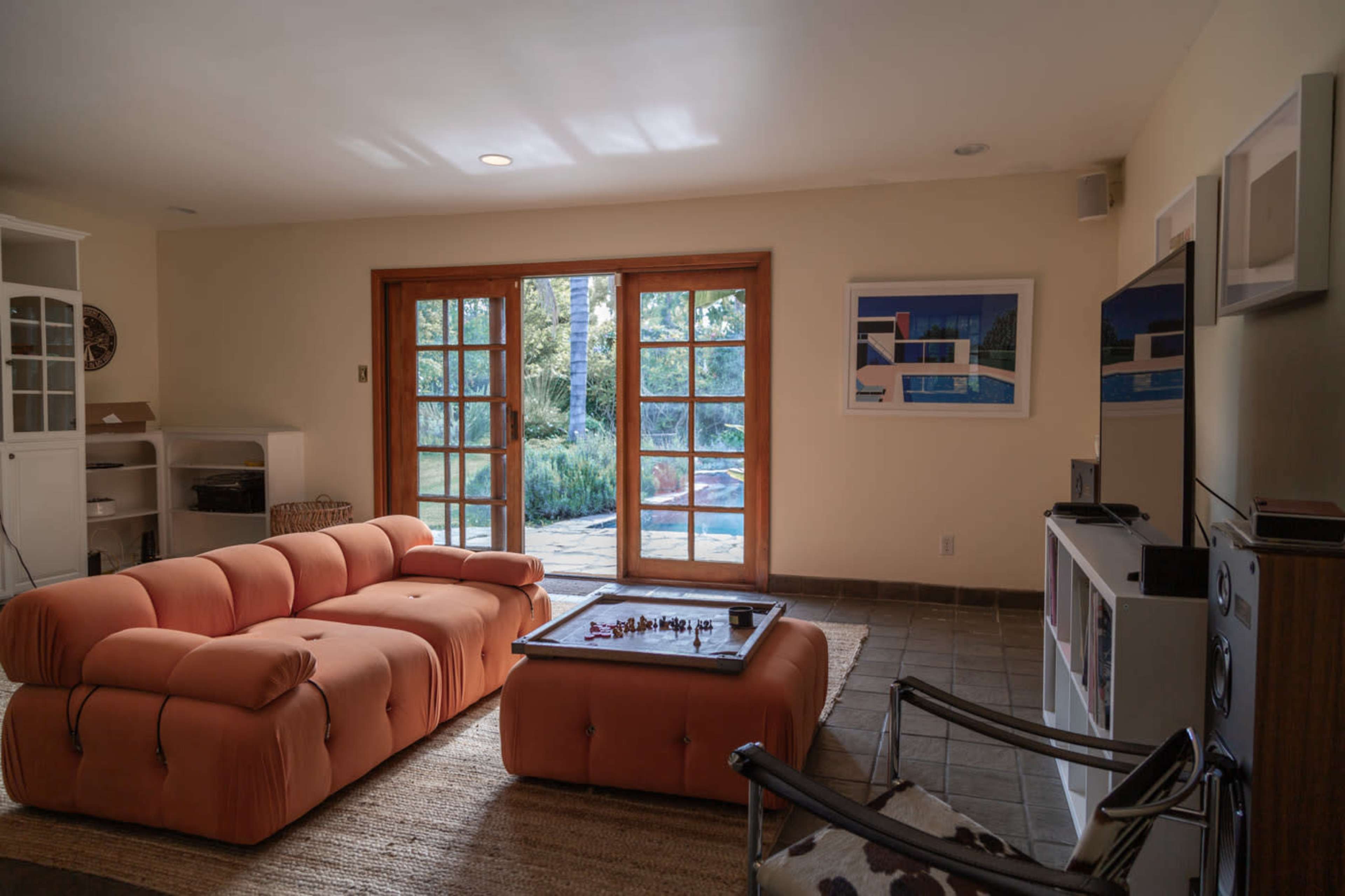 A bright living room features a peach-colored sofa and a glass-top coffee table with a chess set, set against a backdrop of large double doors leading to a patio.