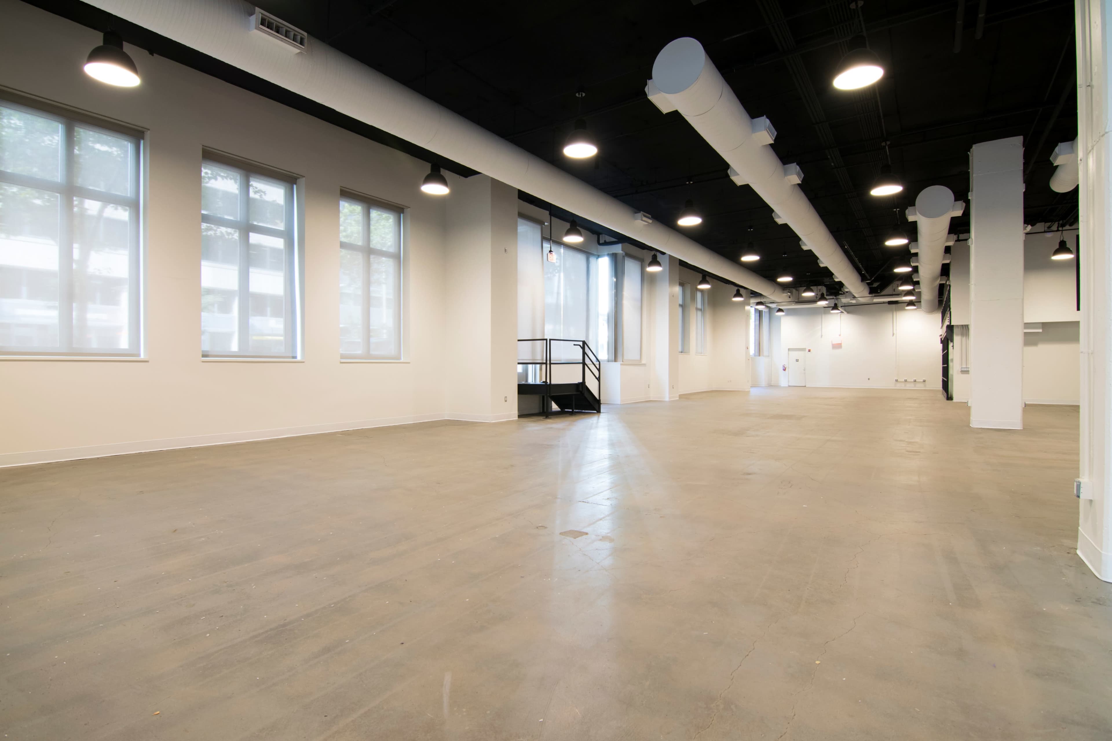An empty, spacious interior with concrete flooring and large windows providing natural light.