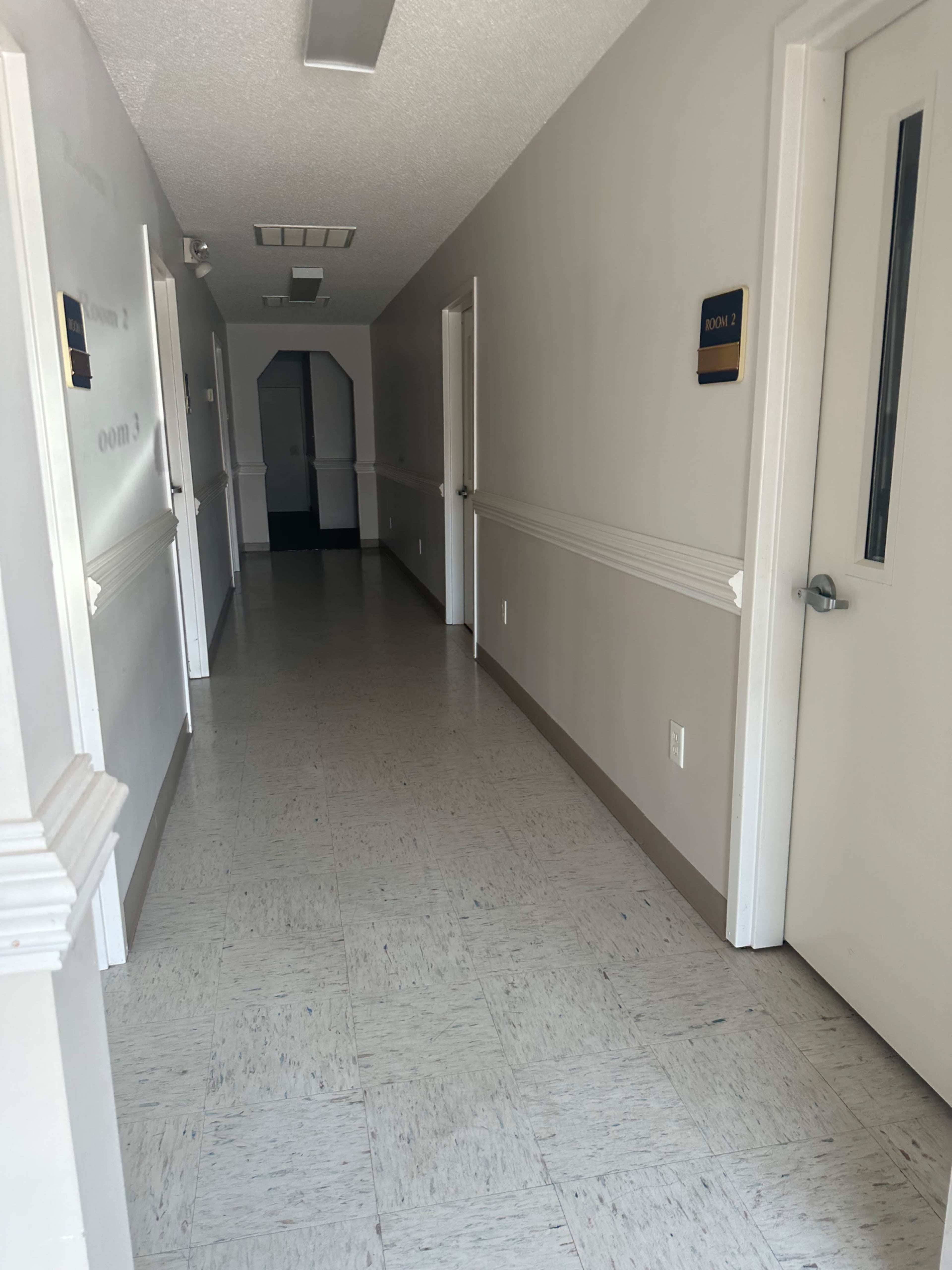 The image shows a long, narrow hallway with closed doors on either side and a doorway at the far end.