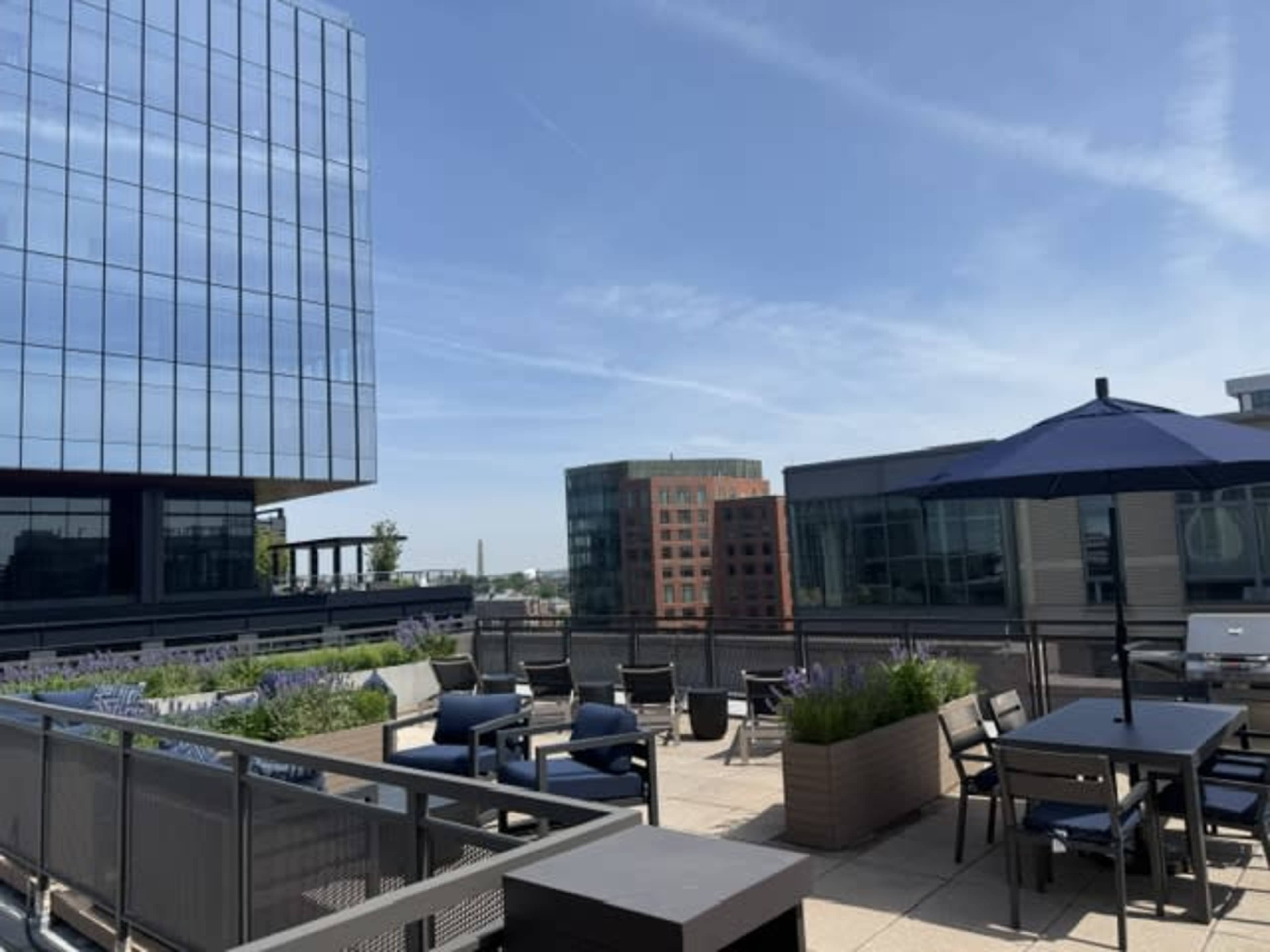 A rooftop terrace features modern seating and tables with a view of surrounding buildings under a clear sky.