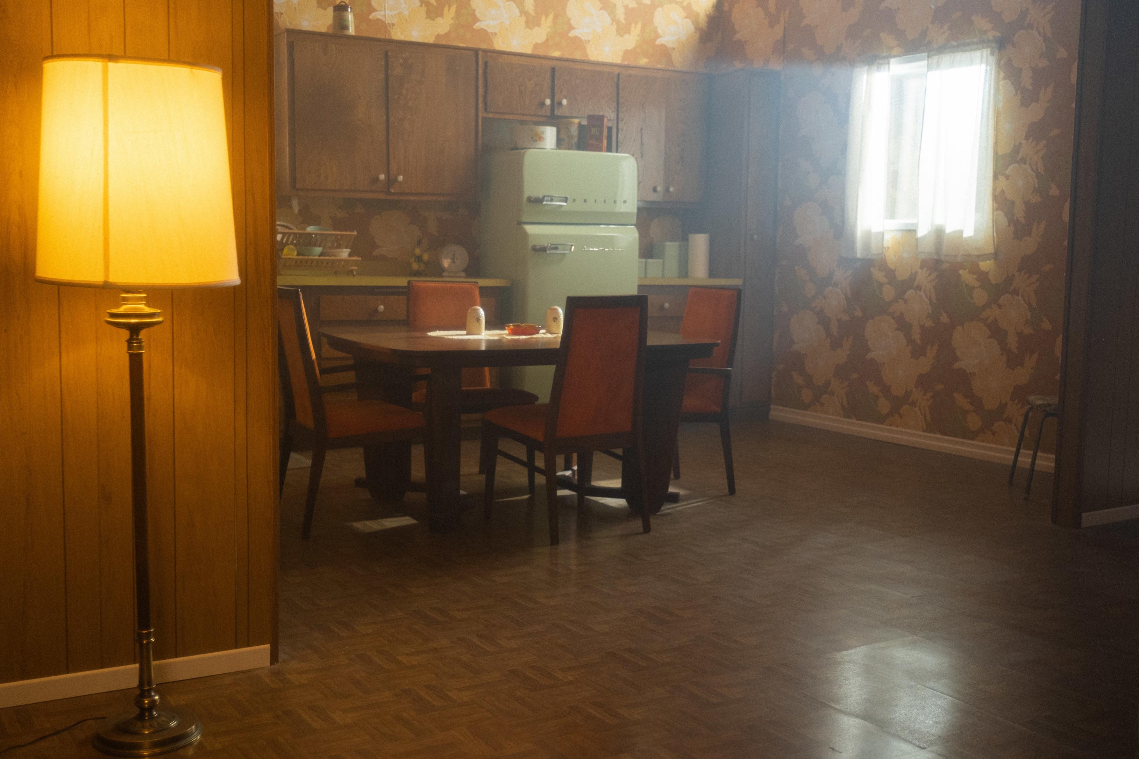 A vintage kitchen with a table set for a meal, surrounded by chairs, and a green refrigerator in the background.