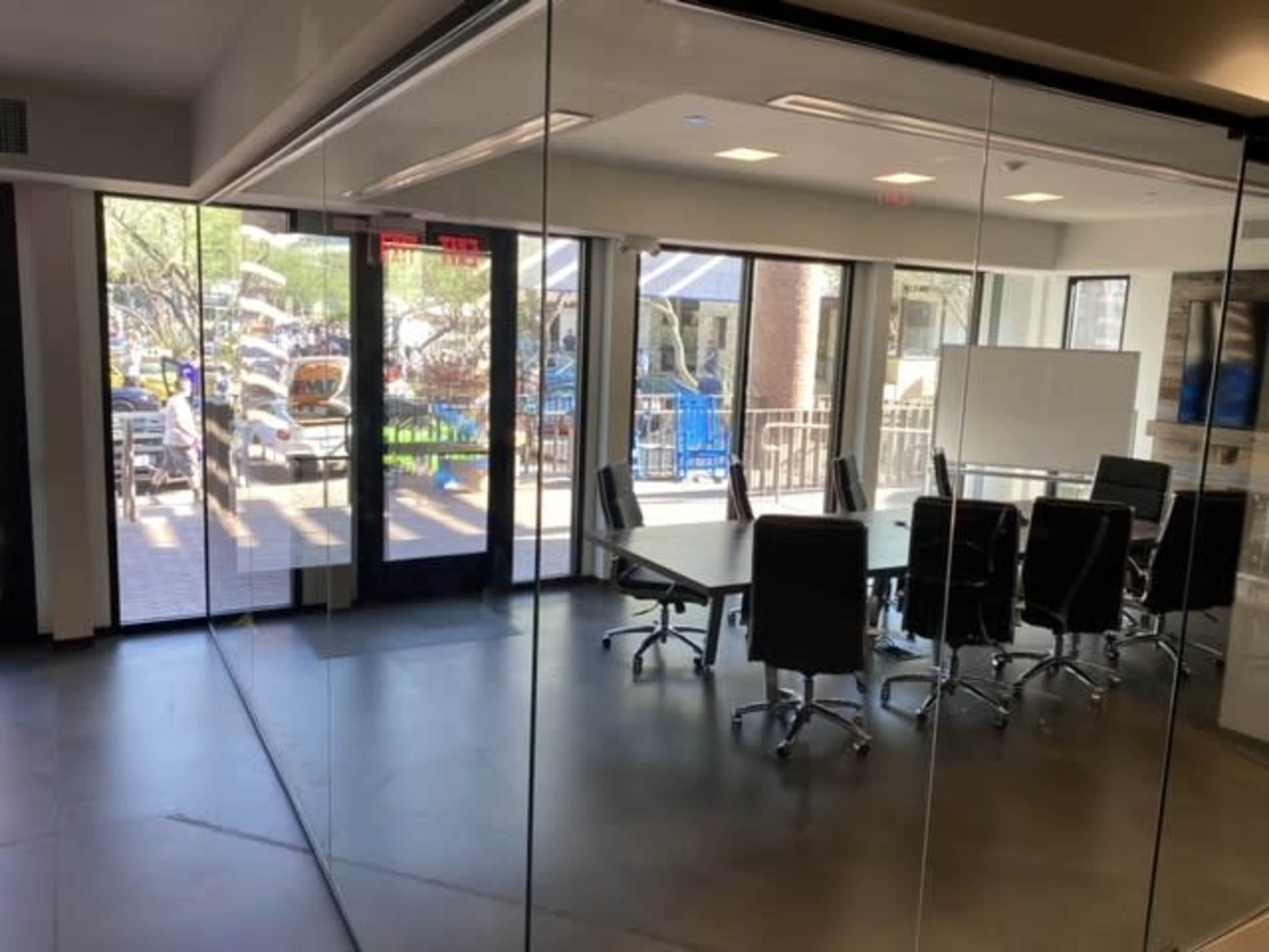 A glass-walled conference room features a long table and chairs, with an outdoor area visible through the large doors.