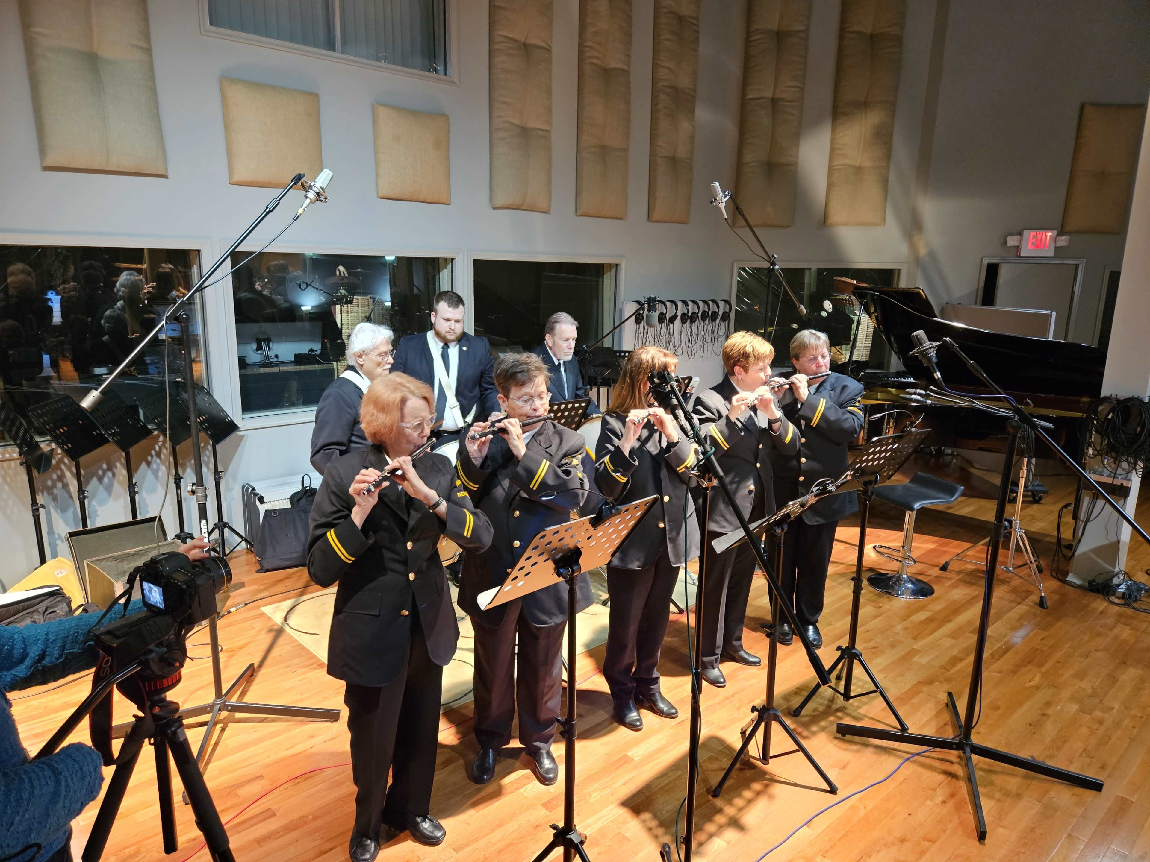 A group of musicians in black jackets plays flutes in a recording studio.