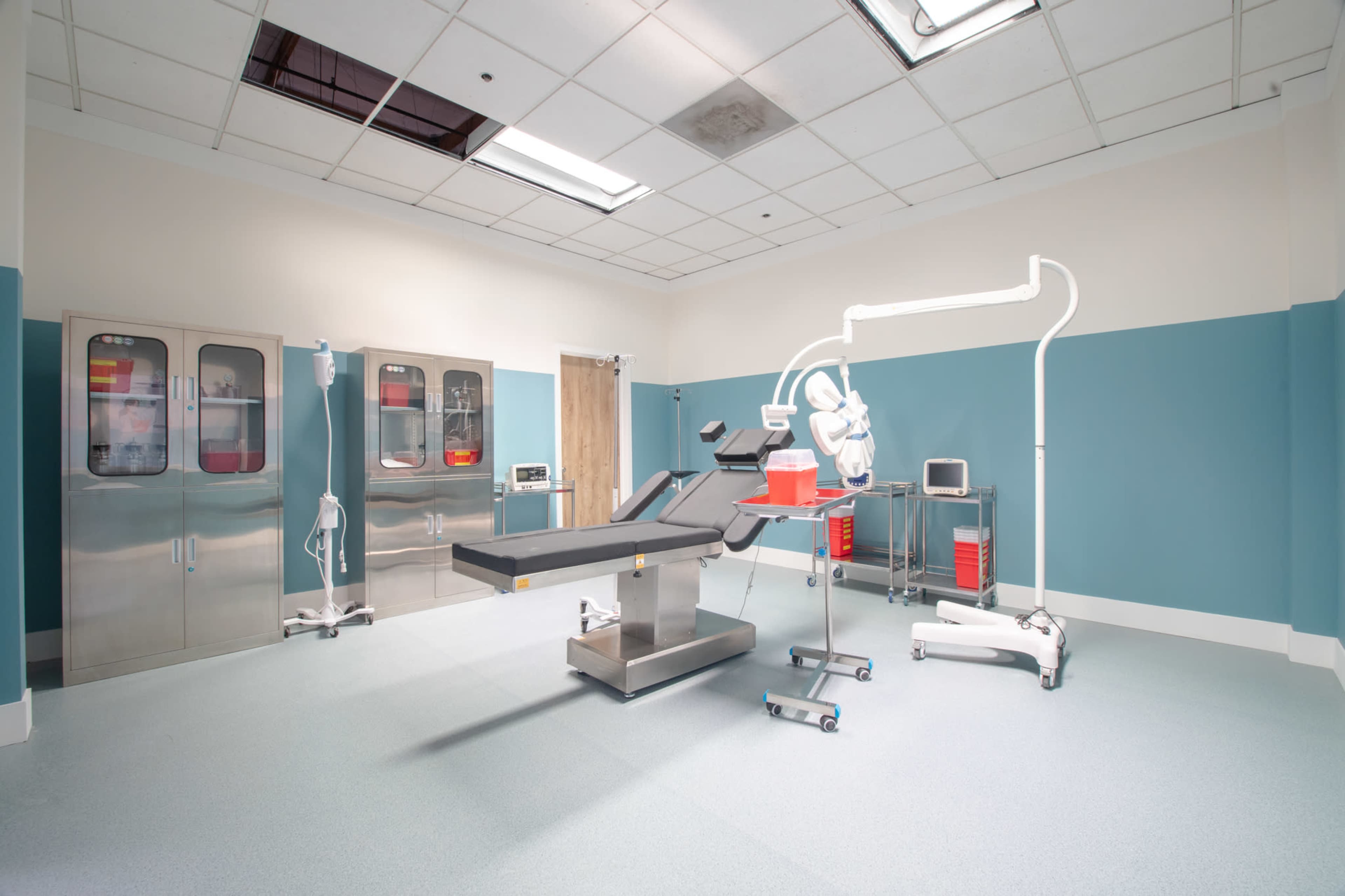 The image shows a sterile medical operating room equipped with surgical furniture and various medical equipment against a muted color scheme.