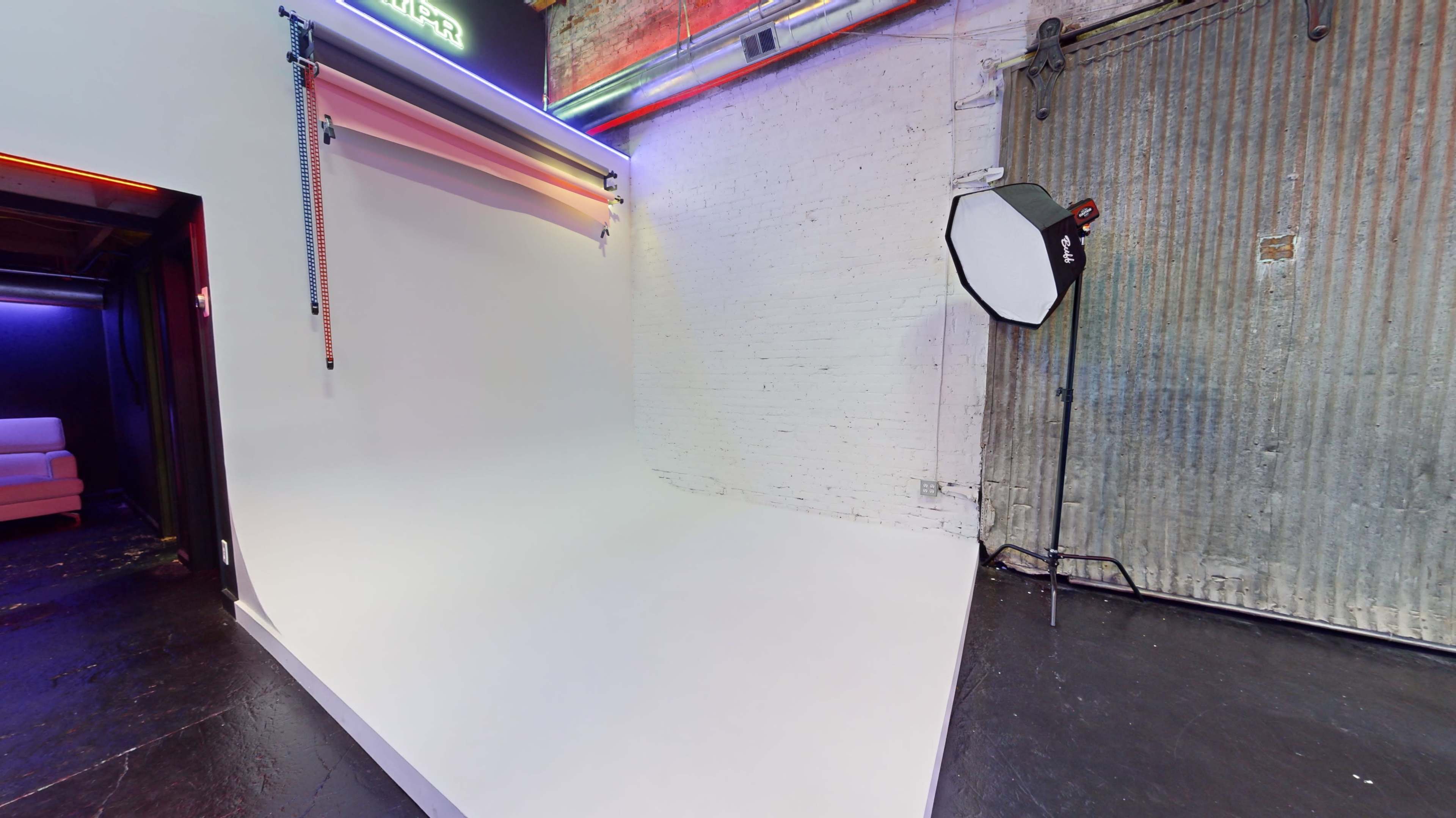 A photography studio with a seamless white backdrop and a softbox light positioned nearby against a textured wall.