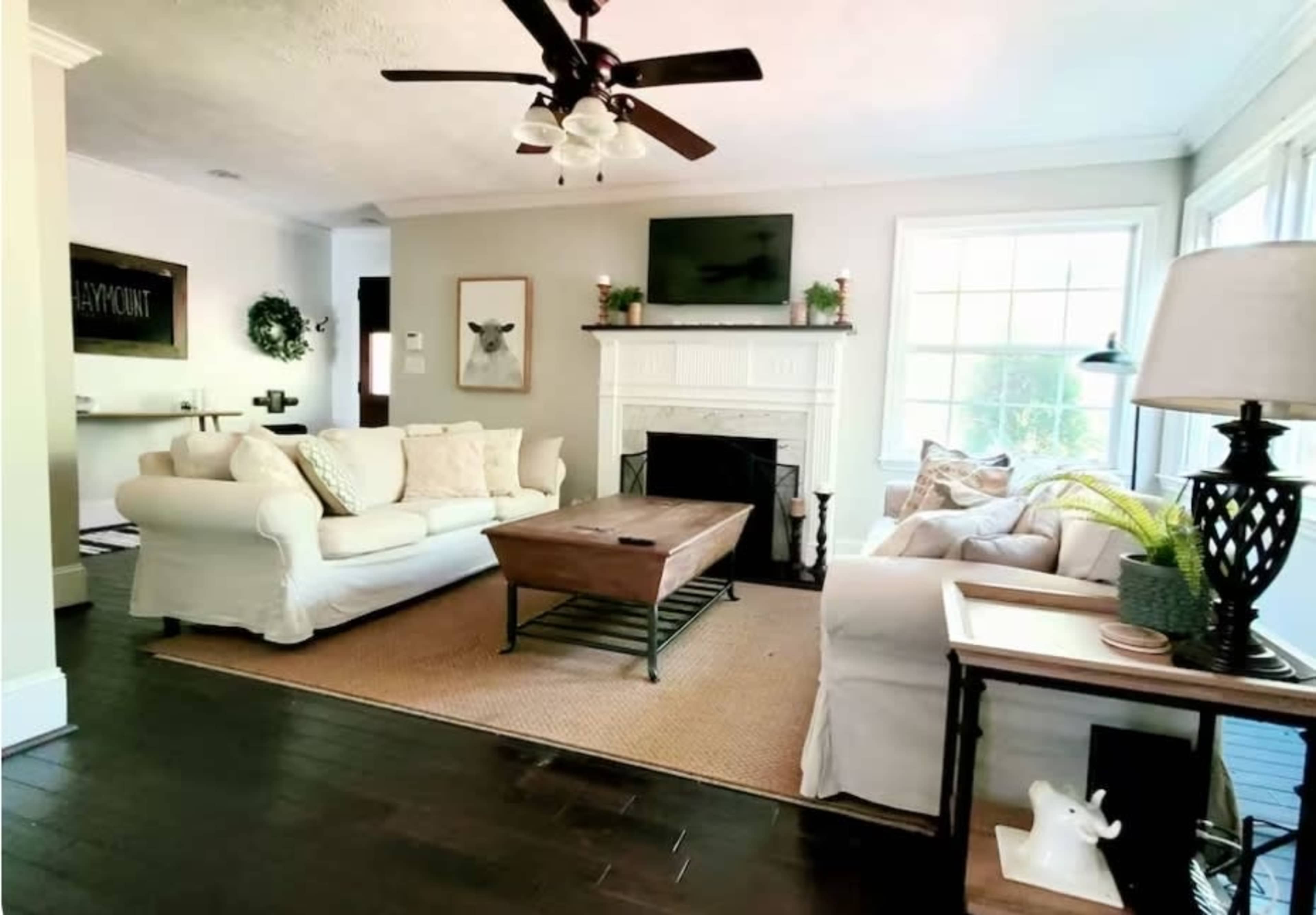 The living room features two sofas, a coffee table, and a fireplace, with natural light streaming through large windows.