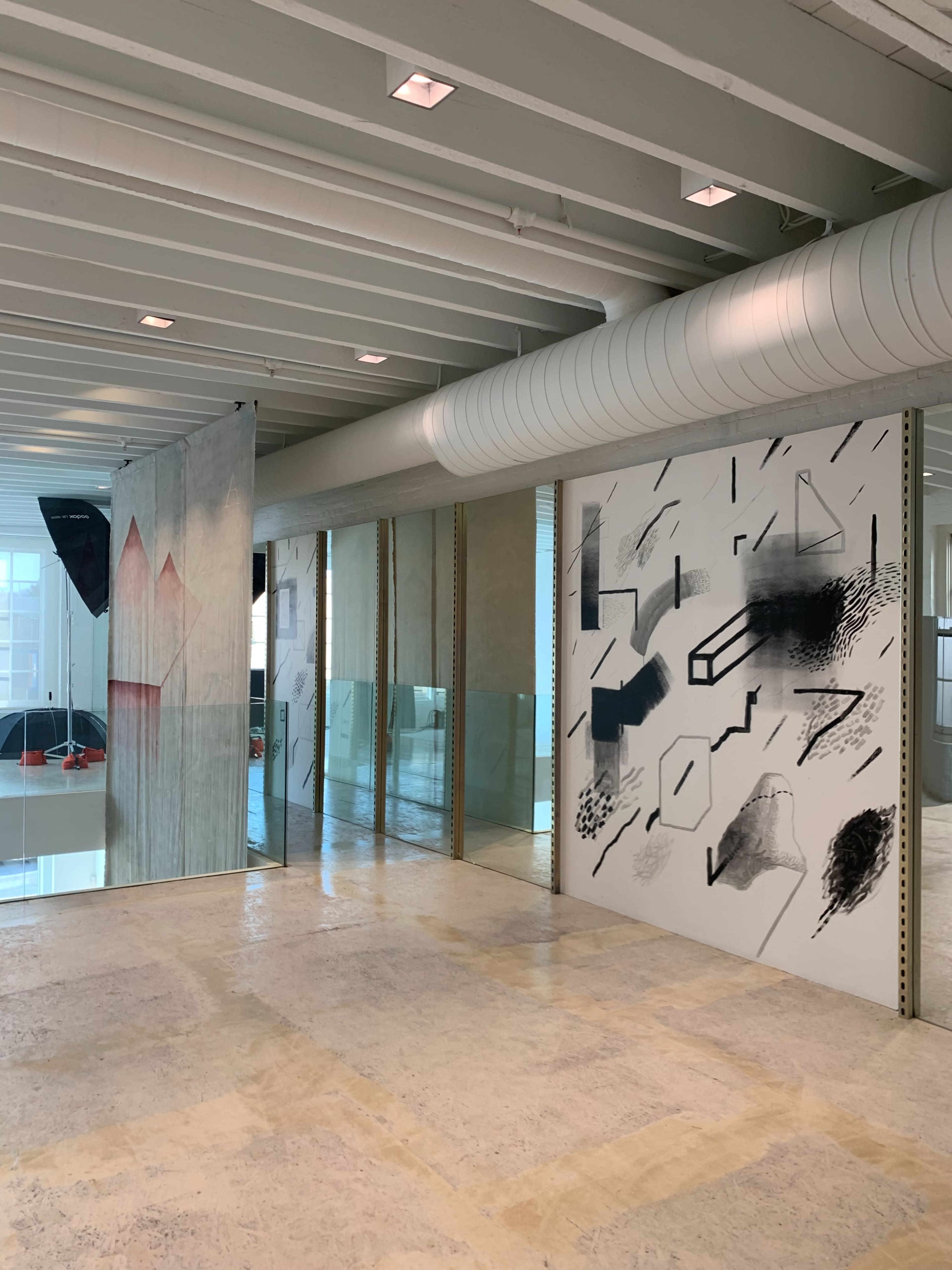 The image shows an interior space featuring abstract wall art and glass walls, illuminated by overhead lights.
