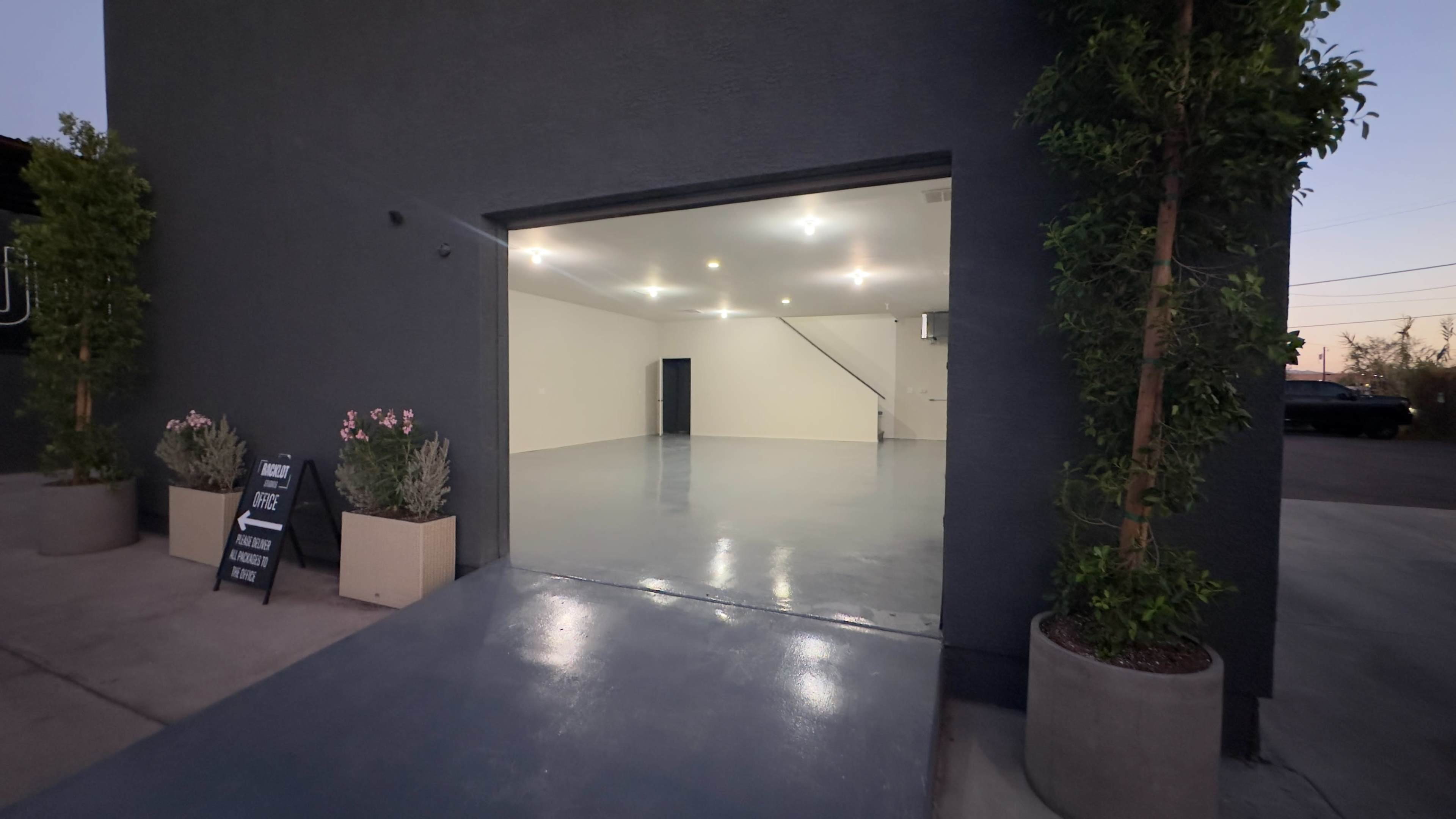An empty garage space with polished concrete floors, bright ceiling lights, and two planters on either side of the entrance.