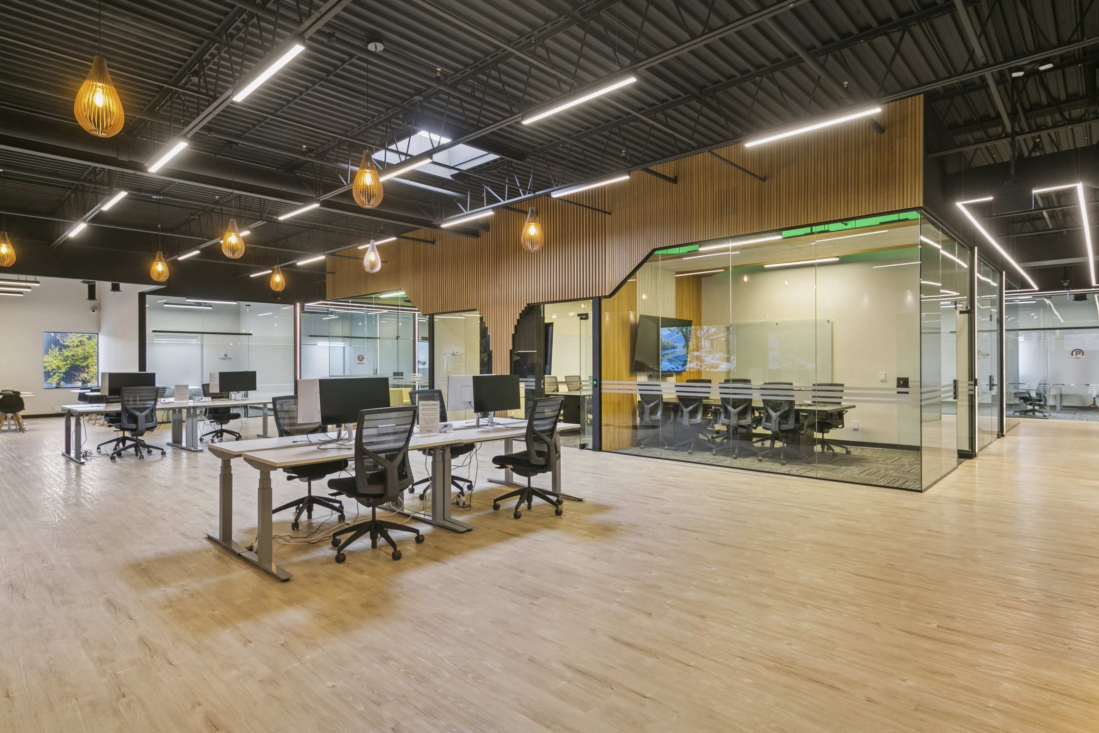 The image shows a modern office space featuring several workstations with ergonomic chairs, large glass meeting rooms, and decorative pendant lighting.