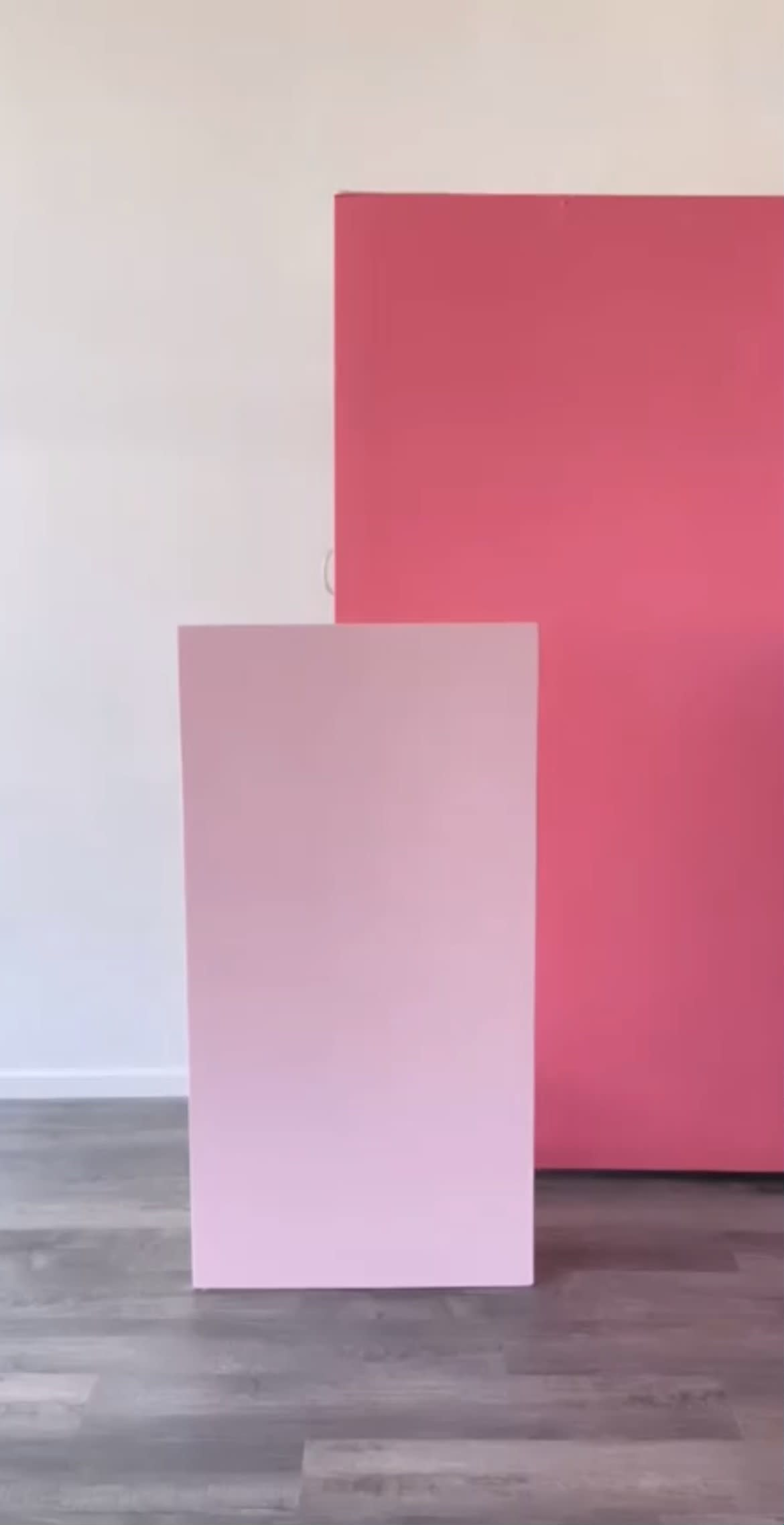 The image shows two pink rectangular panels against a light-colored wall, with one panel positioned upright and the other leaning behind it.