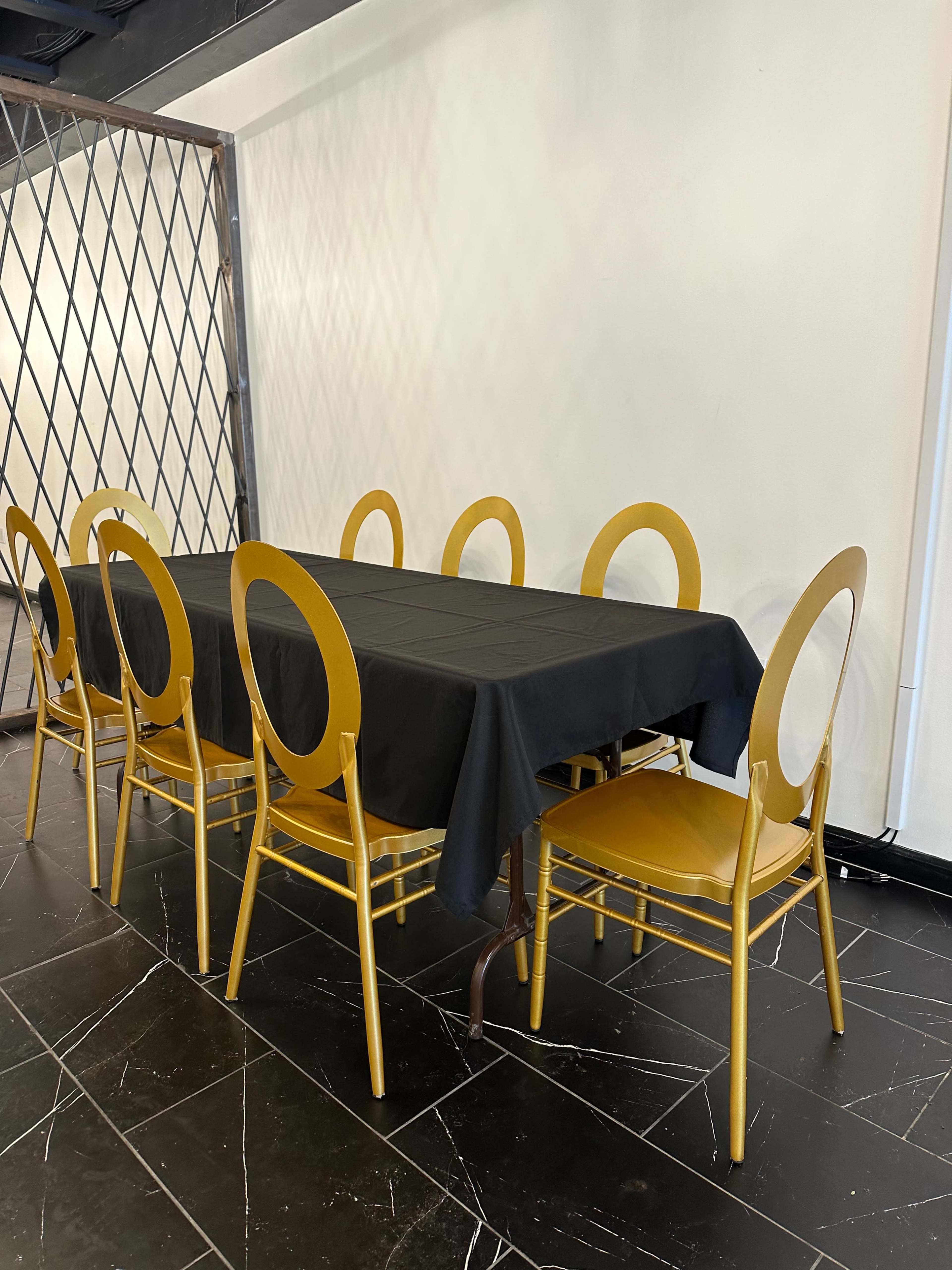 A long black table is set with gold chairs in an empty room.