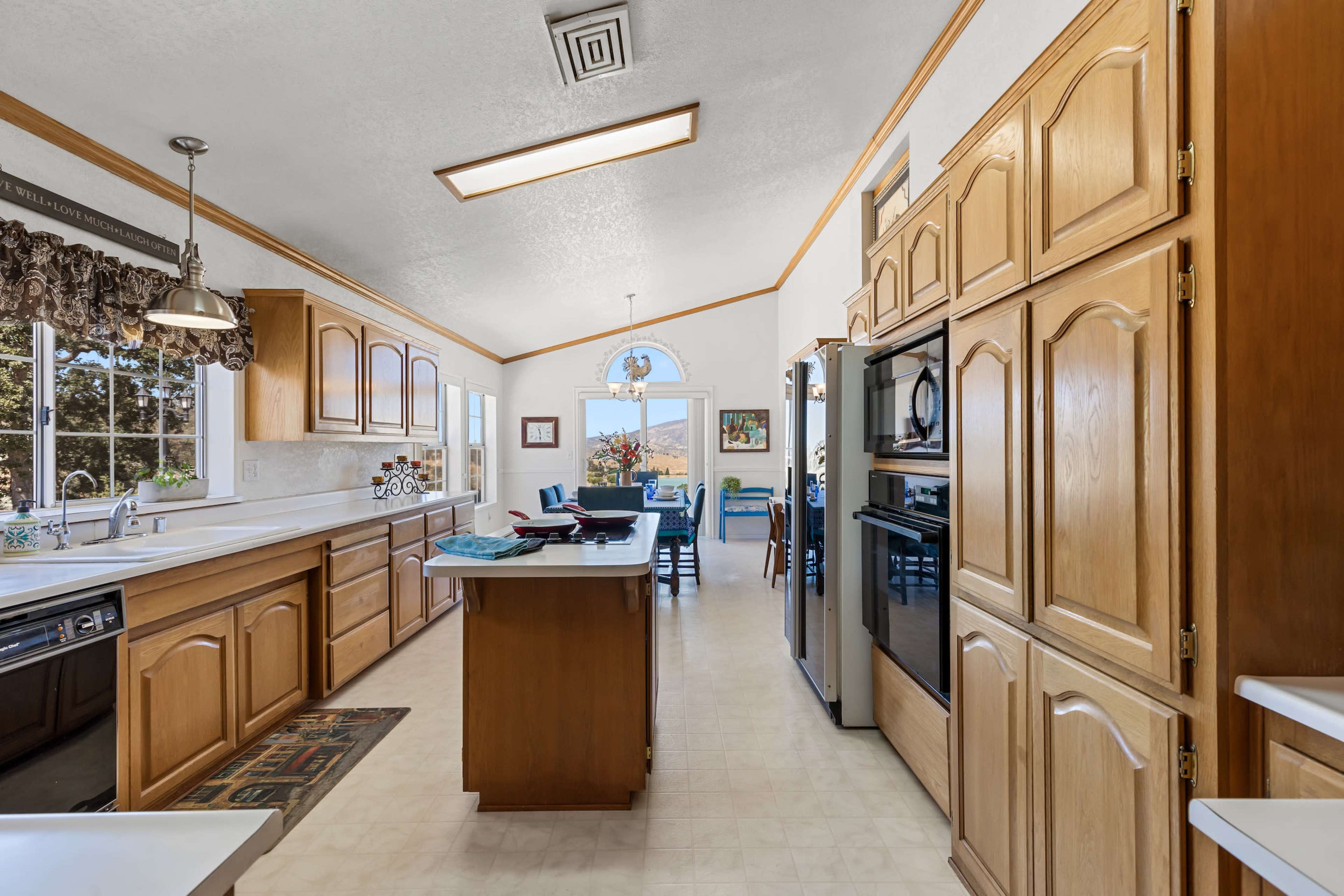 A spacious kitchen with wooden cabinets, a central island, and large windows allowing natural light to enter.