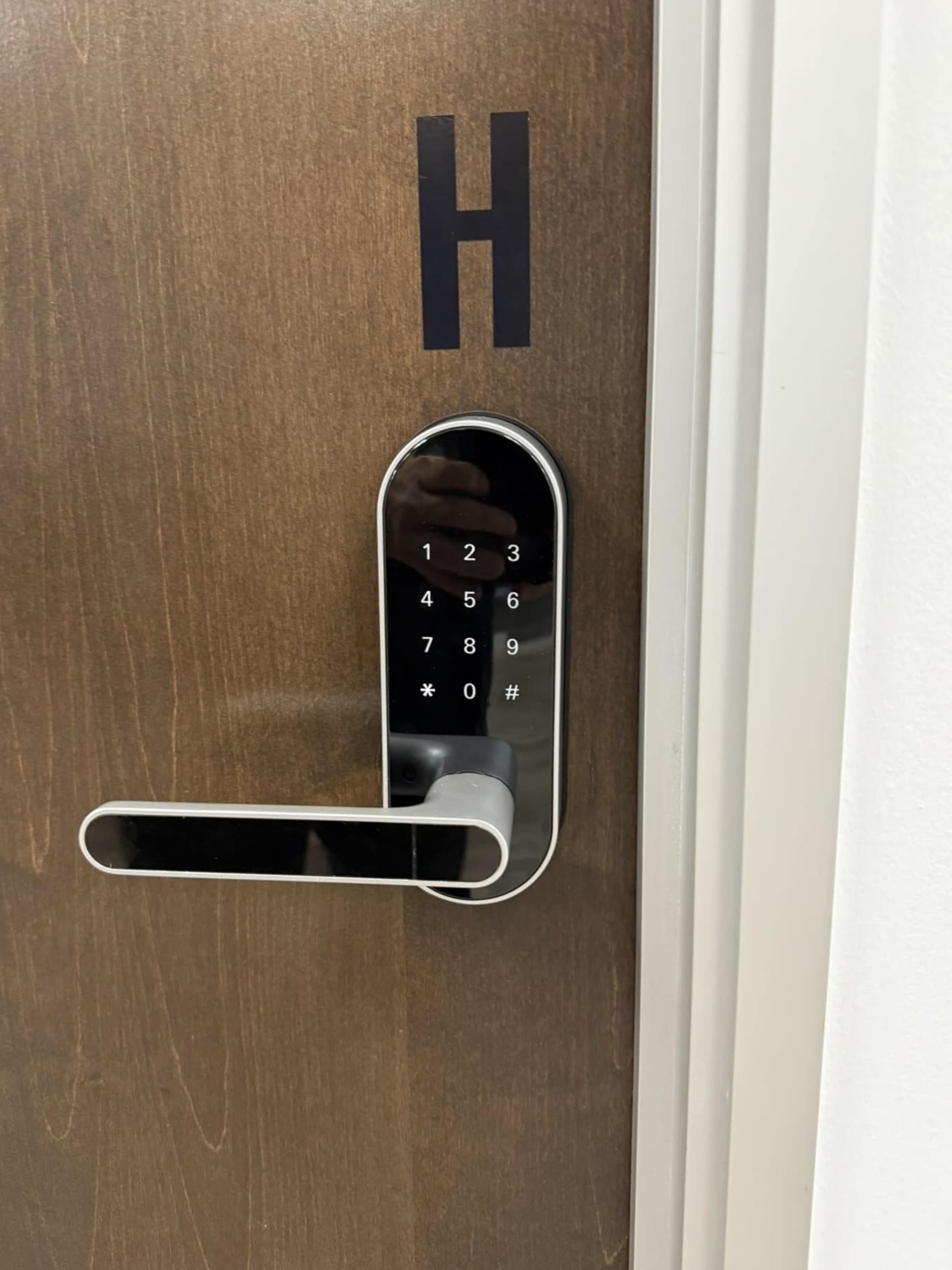 The image shows a wooden door with a digital keypad lock and an "H" label above it.