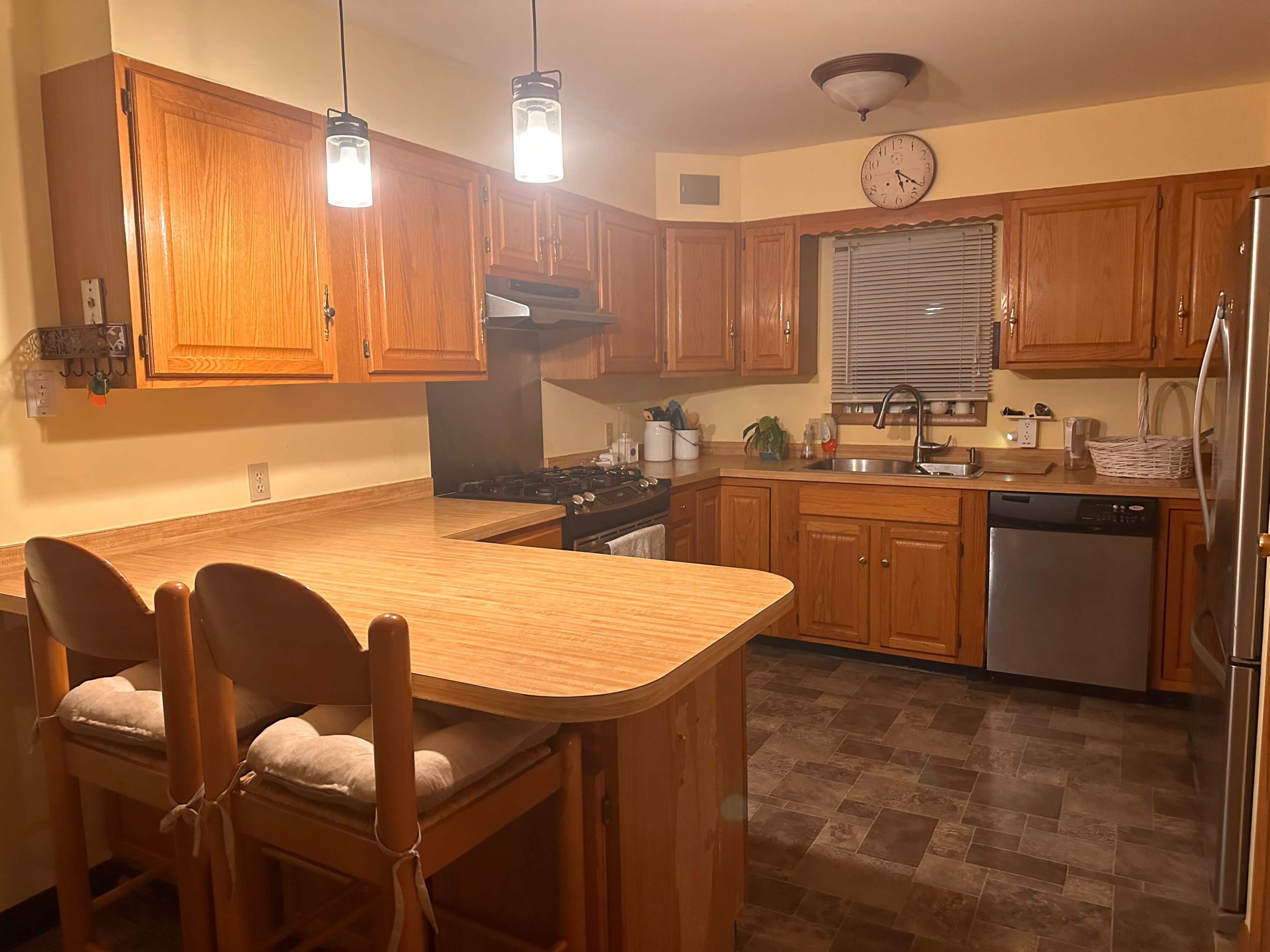 A modern kitchen with wooden cabinets, a central island with seating, and stainless steel appliances.