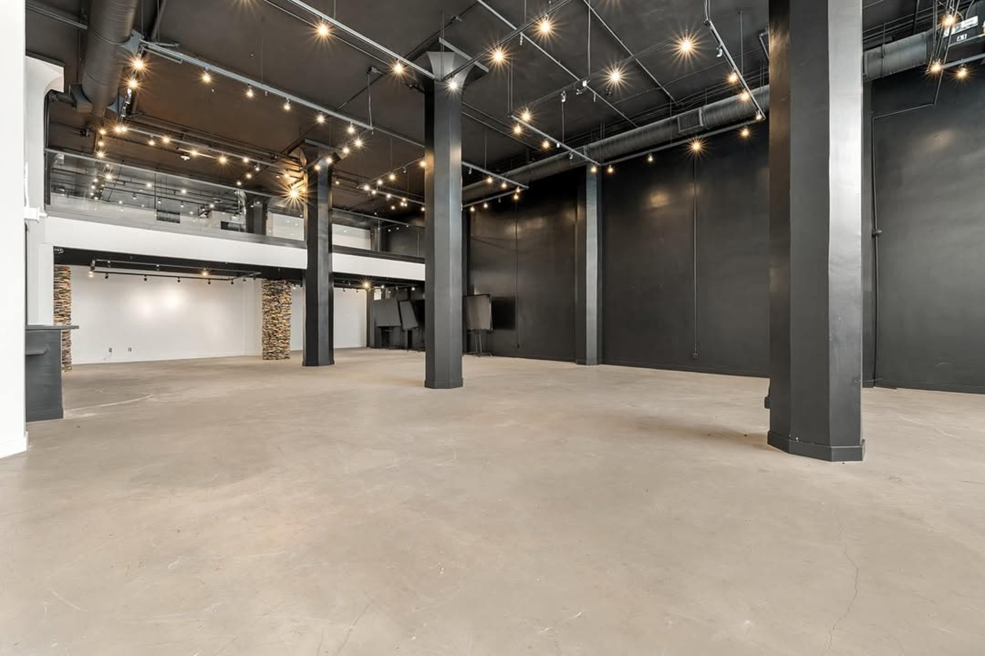 The image features a spacious, empty commercial interior with exposed beams and black walls, highlighted by industrial-style lighting.