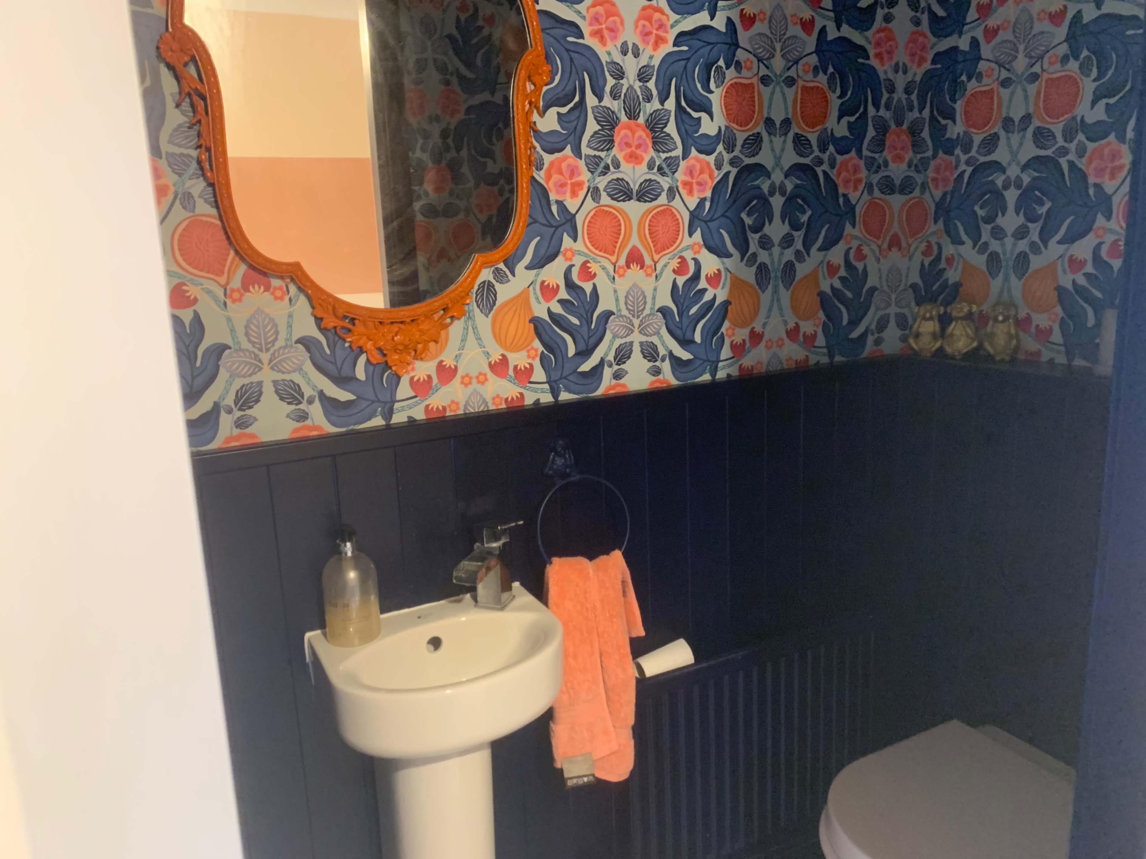 The image shows a bathroom featuring a floral patterned wallpaper, a round mirror, and a white sink with a hand towel hanging beside it.