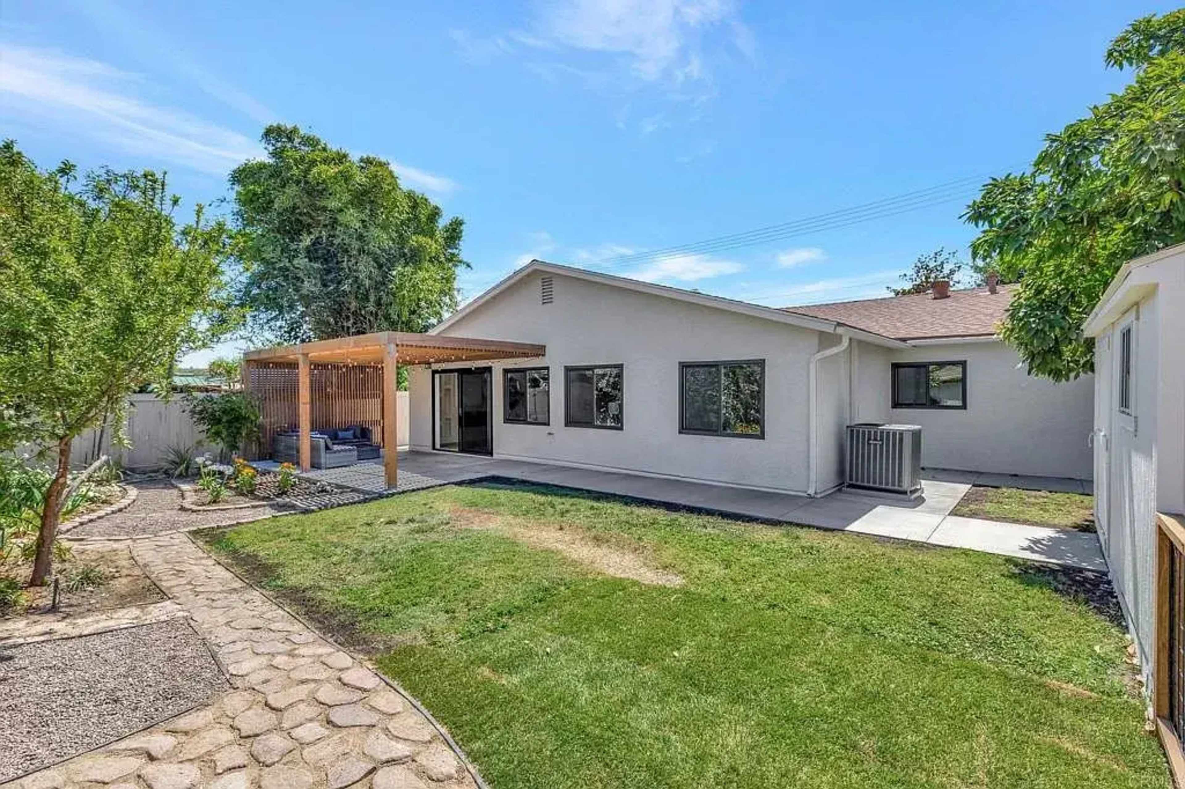 A spacious backyard with a patio, well-maintained lawn, and a pathway leading to a nearby garden area.