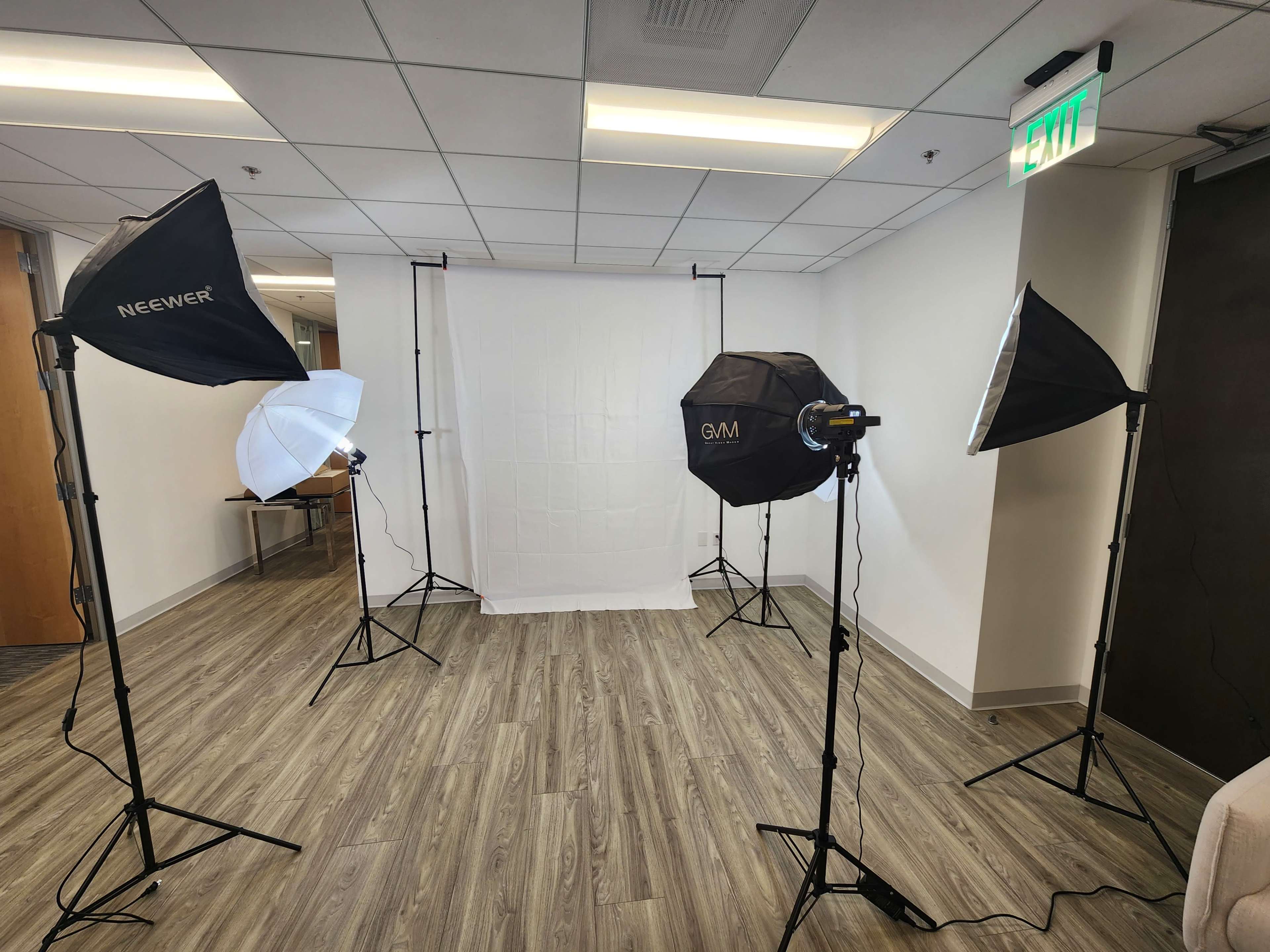 A photo studio is set up with multiple light stands and softboxes surrounding a plain white backdrop.